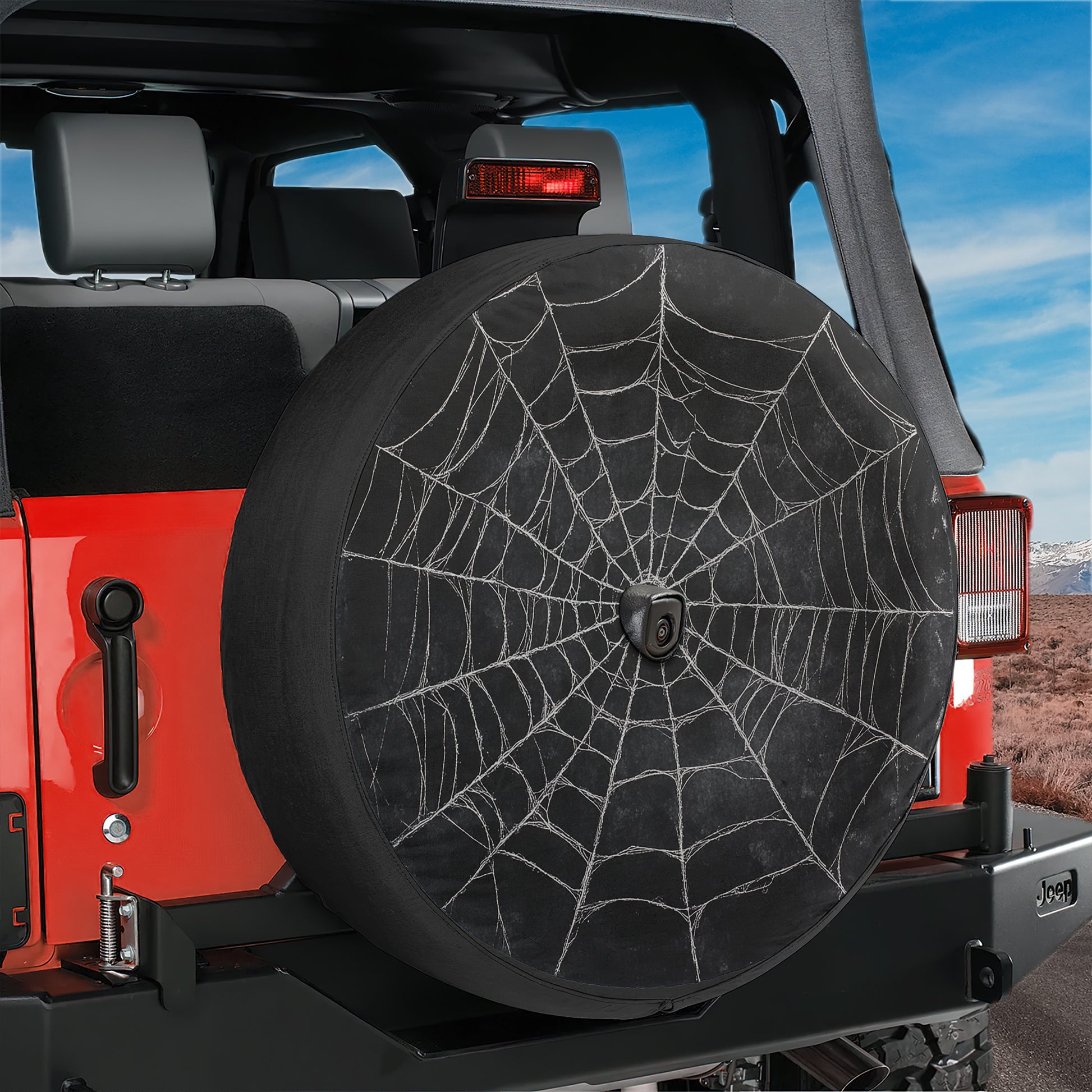 A red Jeep Wrangler with a black spider web-patterned spare tire attached to the rear.