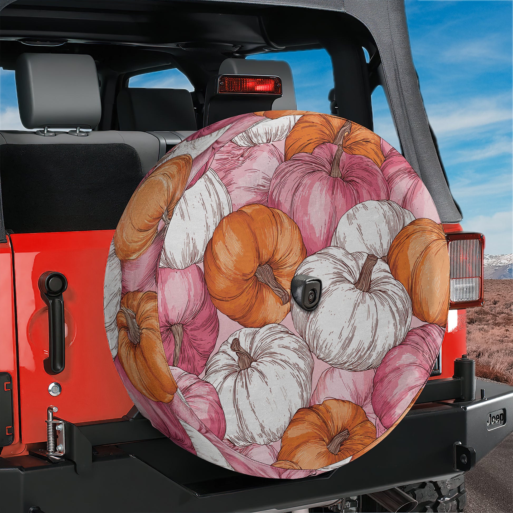 A colorful wheel cover with a pumpkin pattern is attached to the rear of a red Jeep.