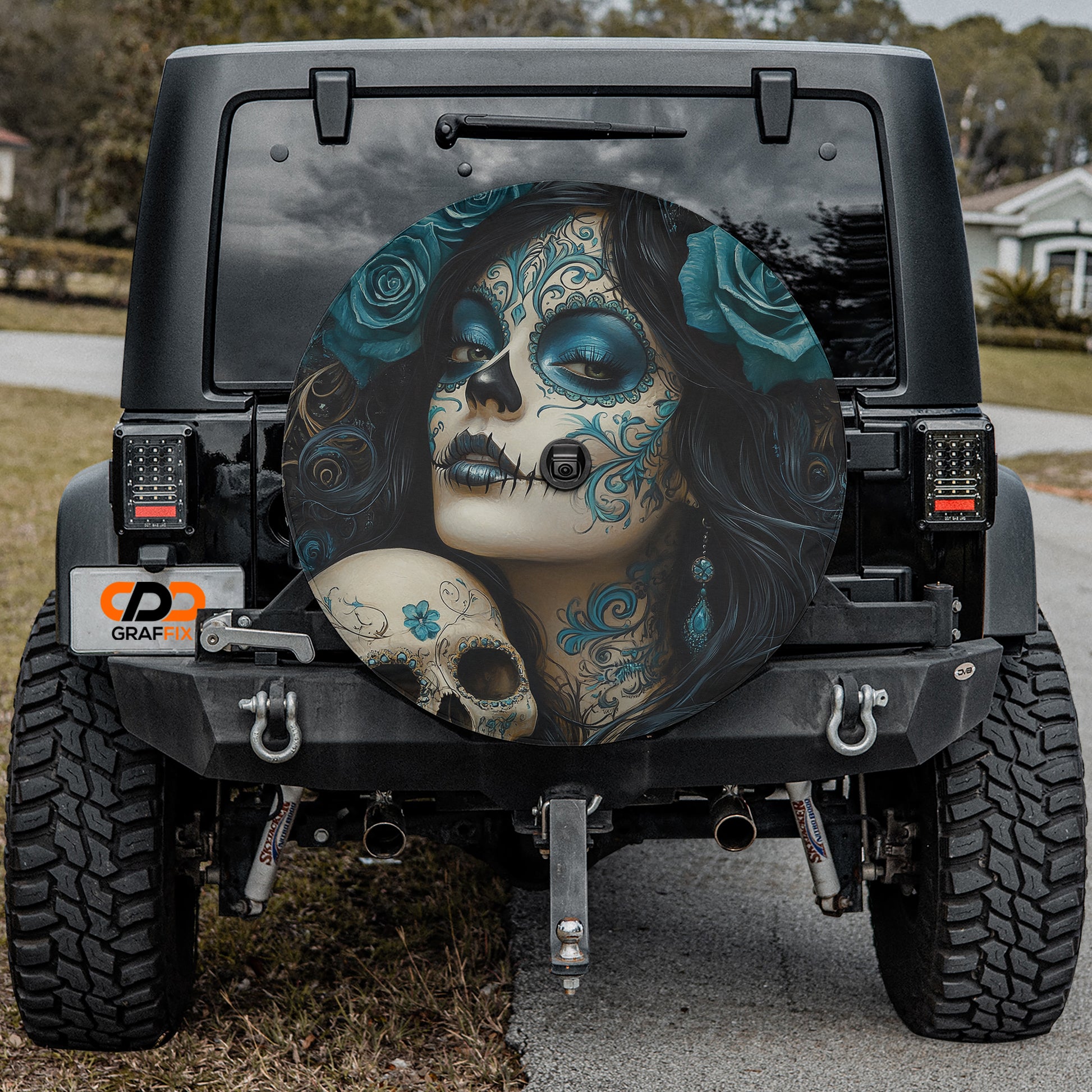 a black Jeep Wrangler with a large, colorful wheel cover depicting a woman's face with intricate floral and skull designs.