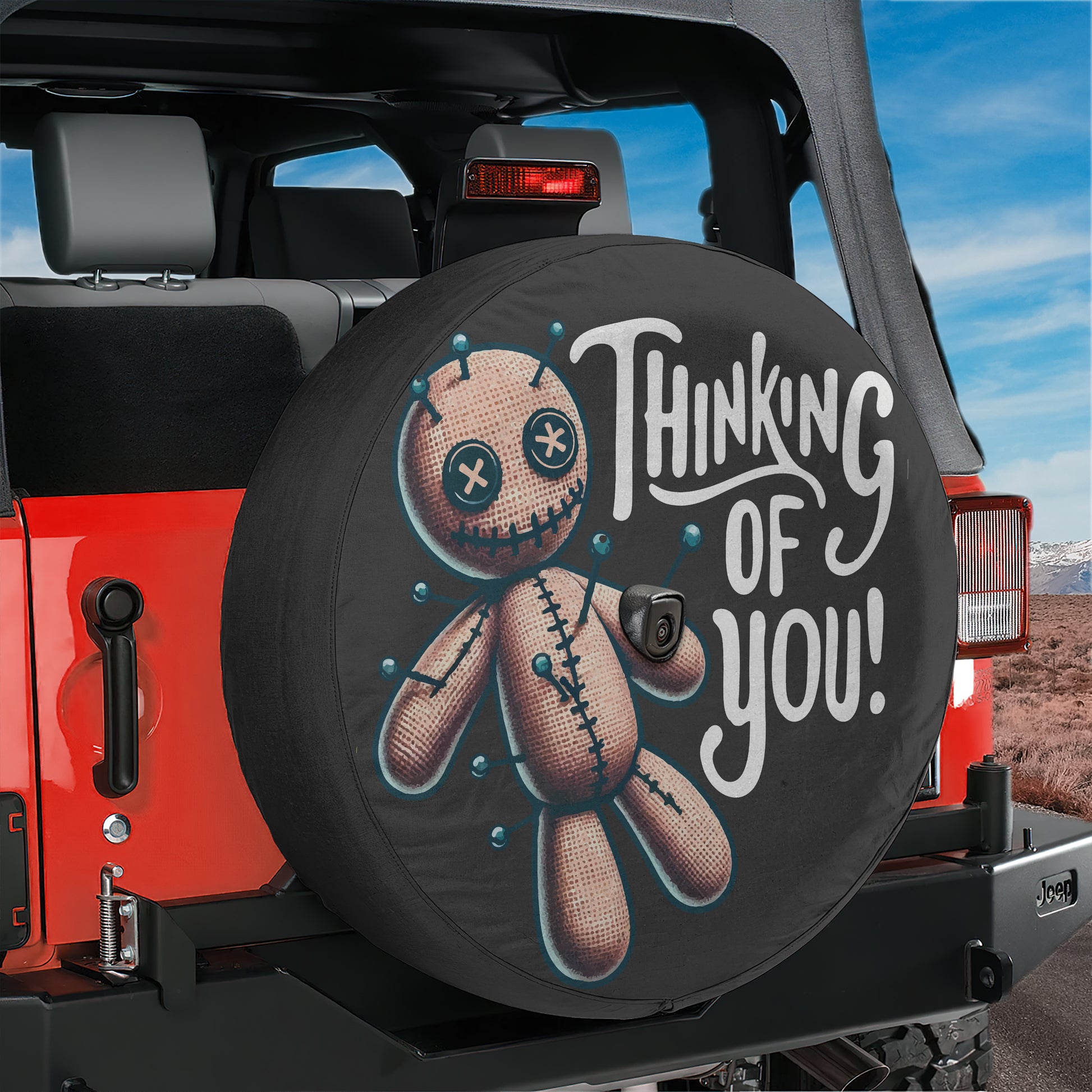 A black tire cover with a cartoon voodoo doll and the text "Thinking of you!" printed on it.