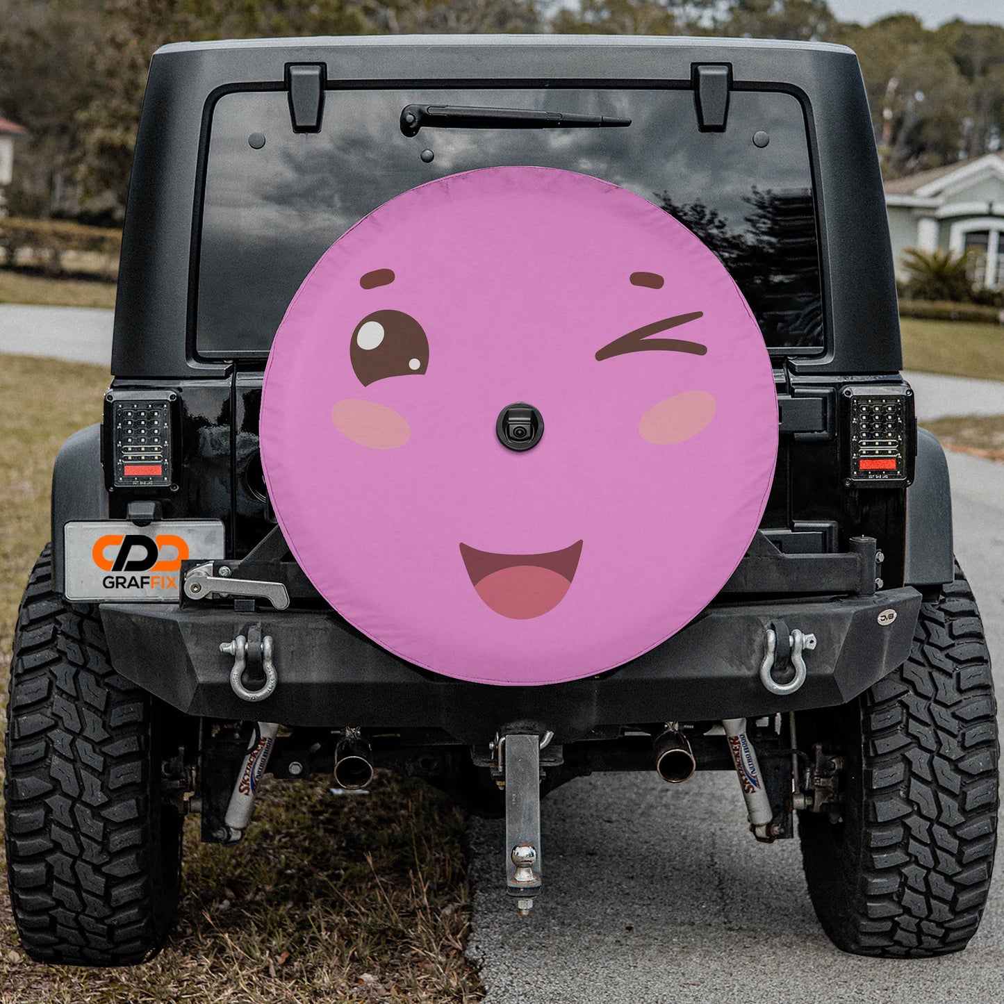 A black Jeep Wrangler with a large, colorful wheel cover featuring a smiling face and a winking eye.
