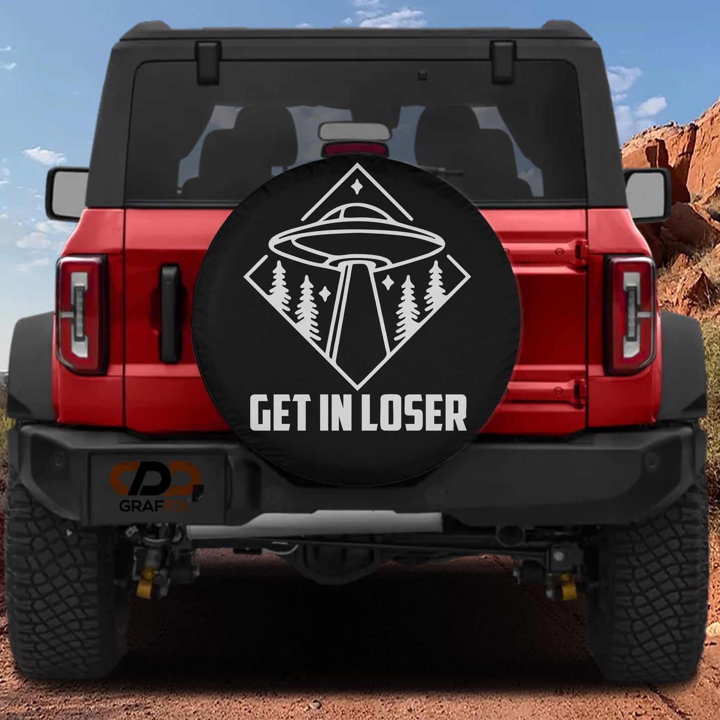 the rear of a red Jeep Wrangler with a large black tire cover featuring a graphic of an alien spacecraft and the text "GET IN LOSER".