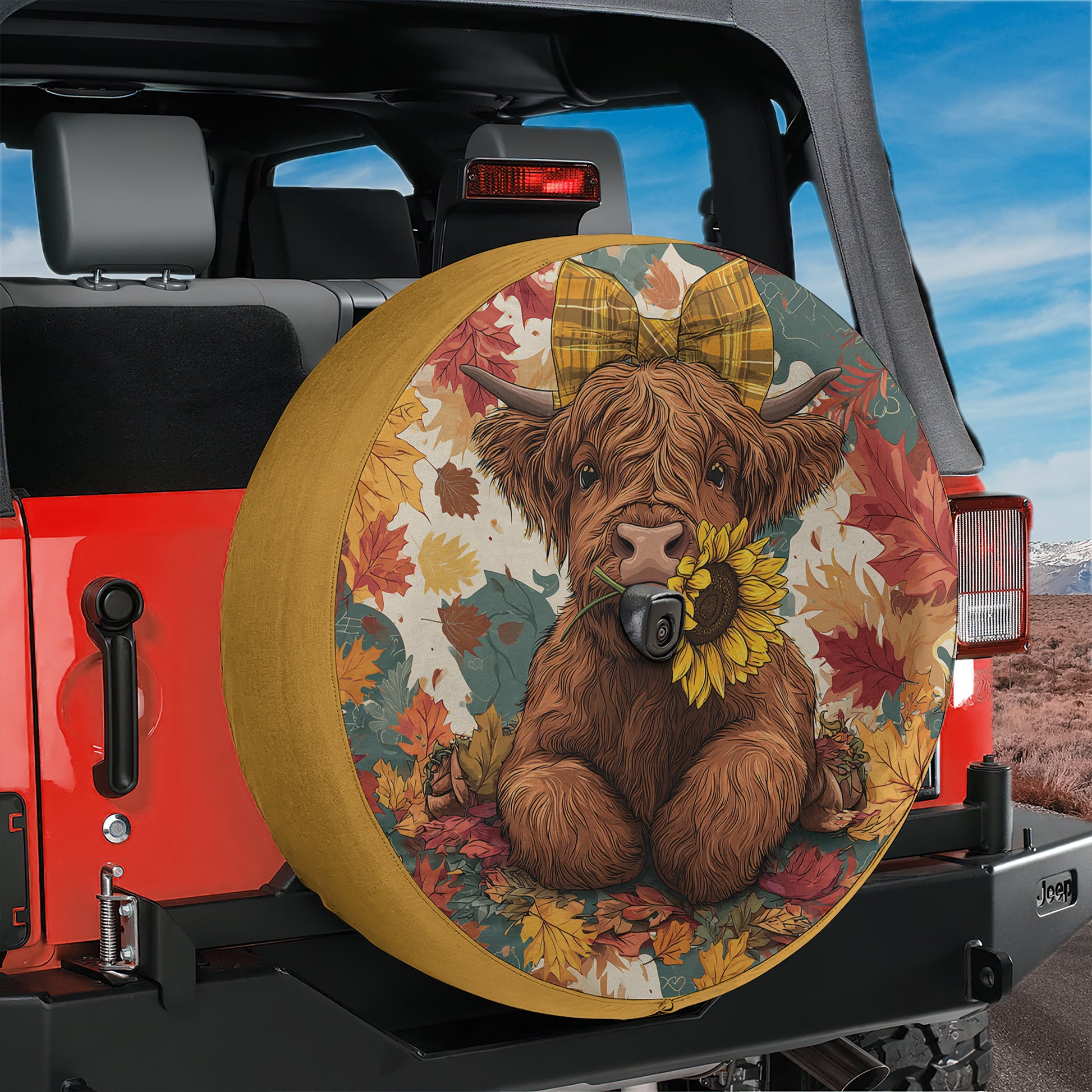 A large, colorful tire cover with a cartoon cow and autumn leaves on it, mounted on the rear of a red Jeep.