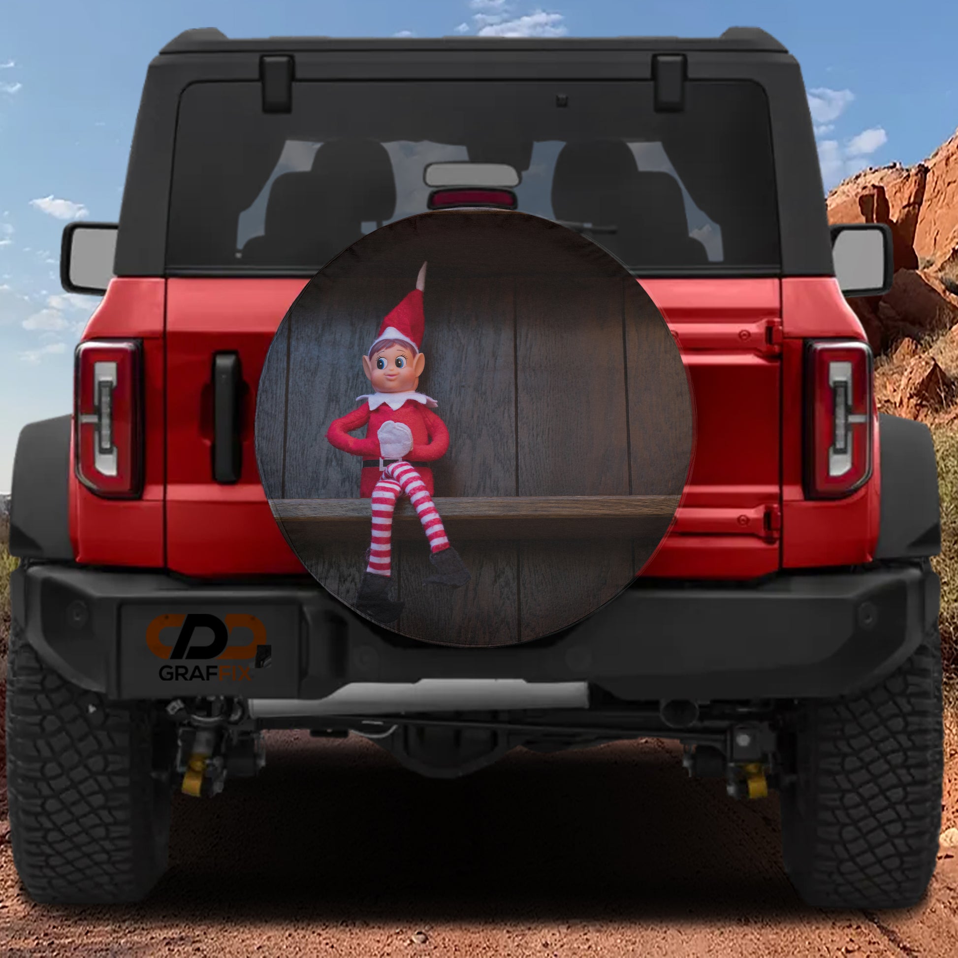 a red Jeep Wrangler with a large round spare tire cover that has a small elf doll on it.