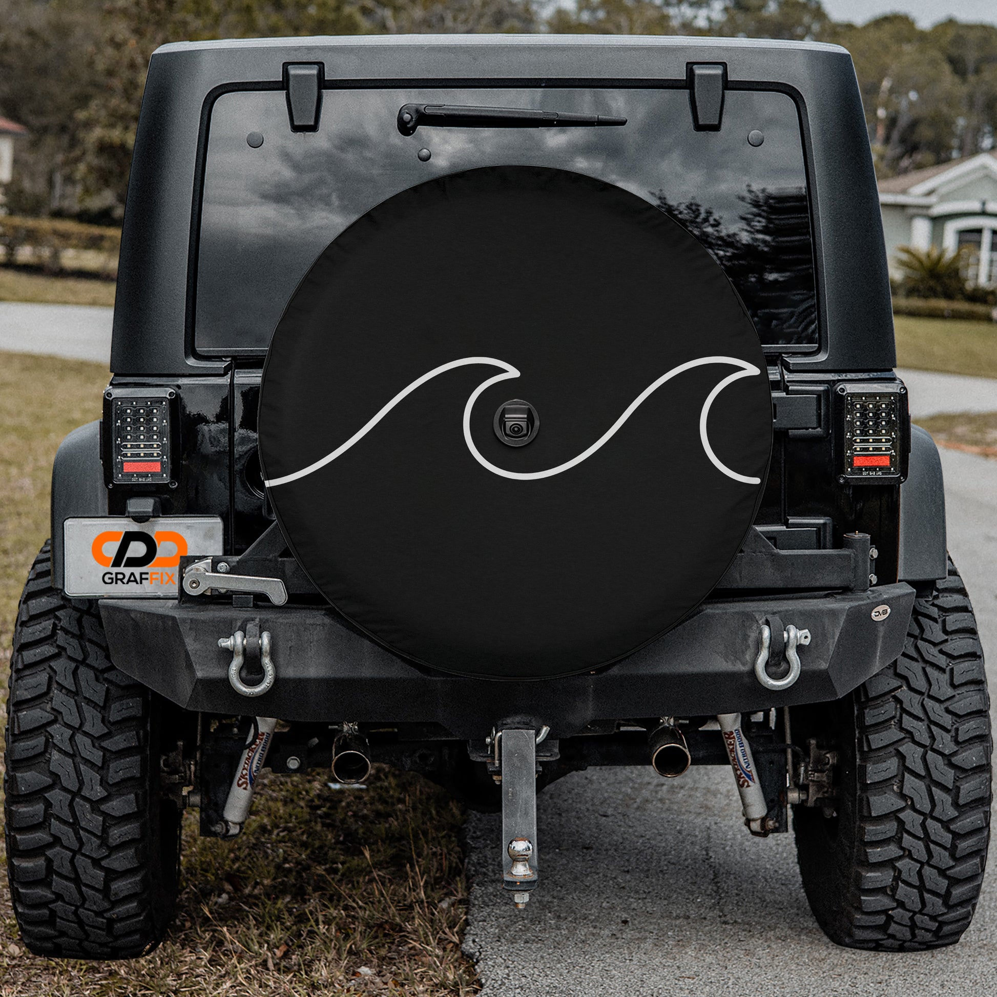 a black Jeep Wrangler parked on a road, with a large black tire cover attached to the rear of the vehicle.