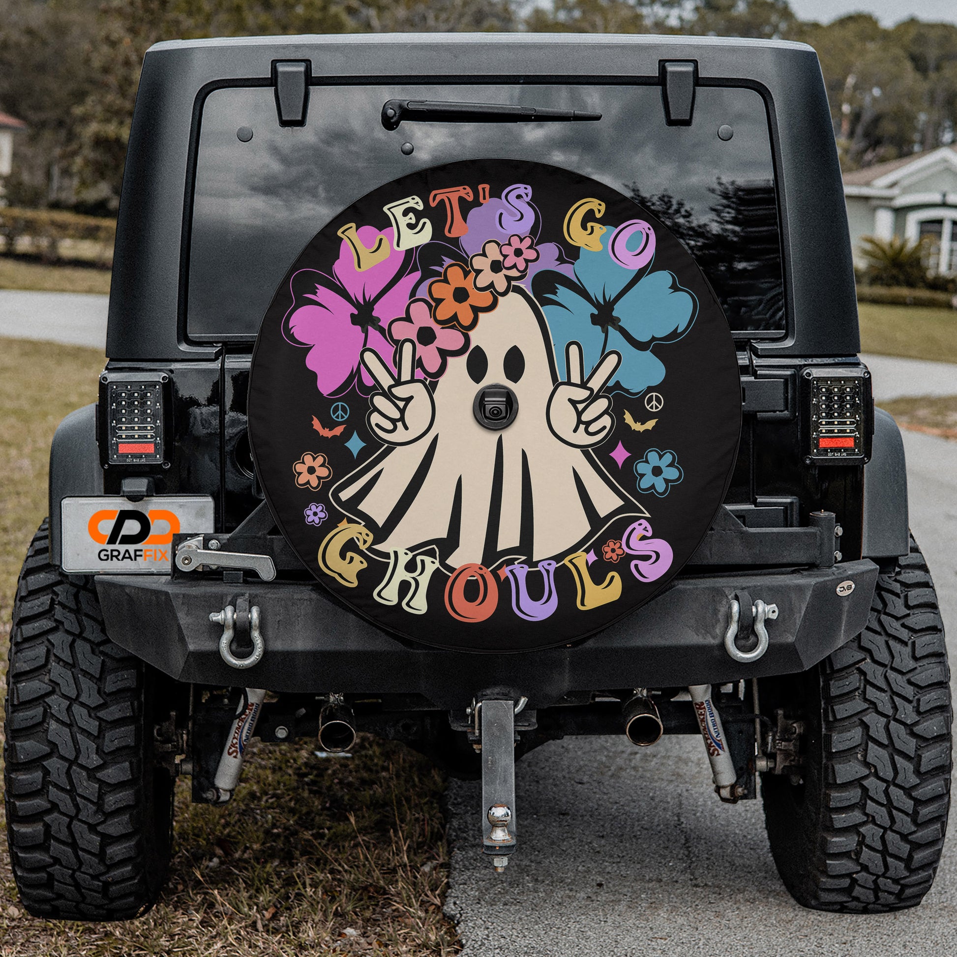 a black Jeep Wrangler with a colorful and whimsical wheel cover that says "LET'S GO GROULS" and includes a ghost character.
