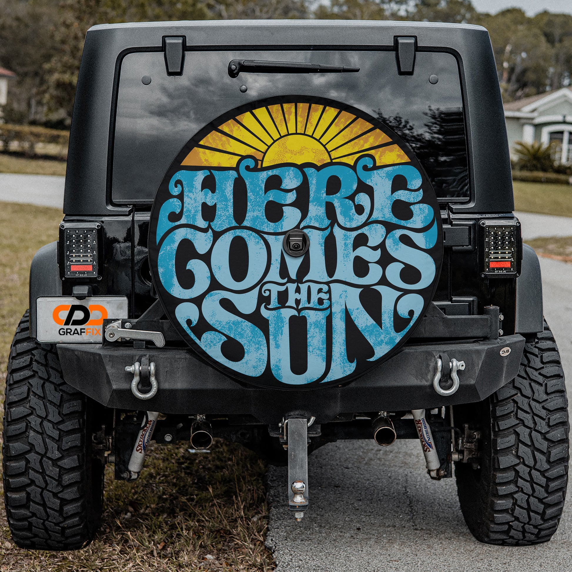 the back of a black Jeep Wrangler with a large, colorful graphic on the rear window that says "HERE COMES THE SUN".