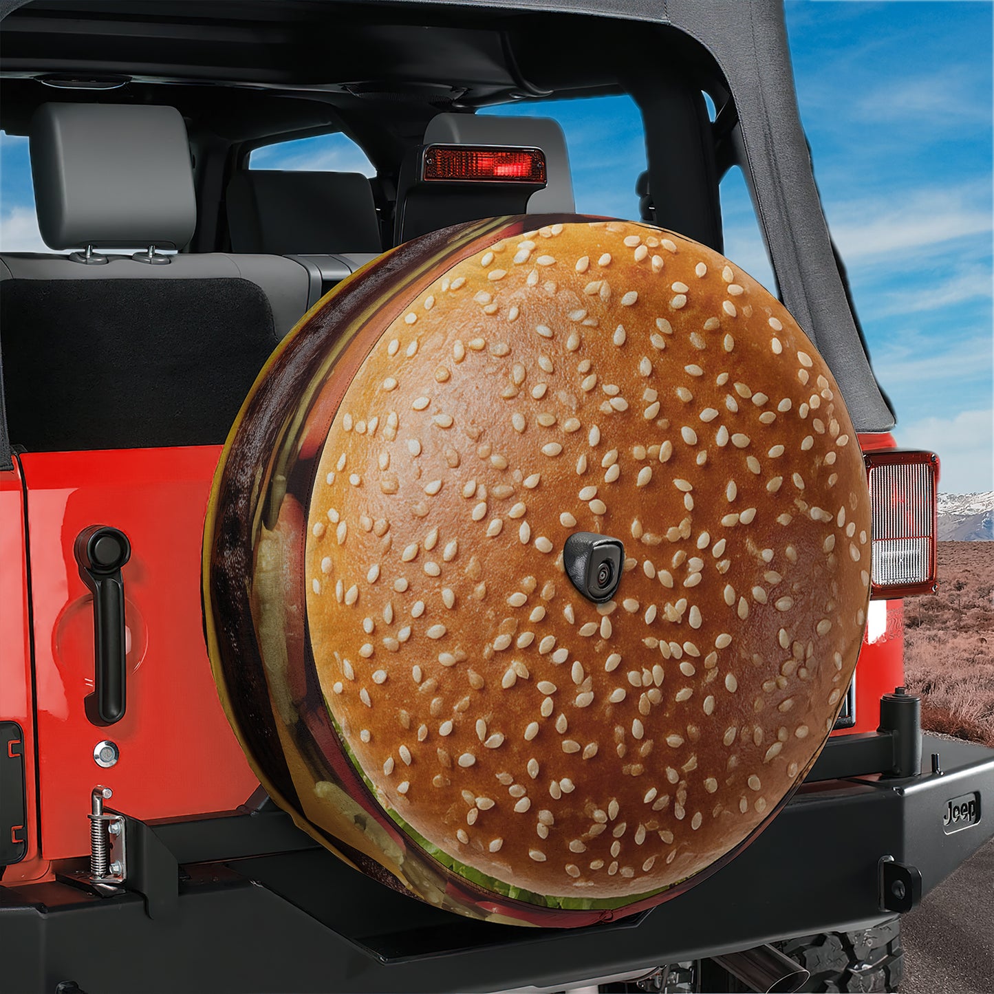 A large hamburger-shaped spare tire is attached to the rear of a red Jeep, with a clear blue sky in the background.