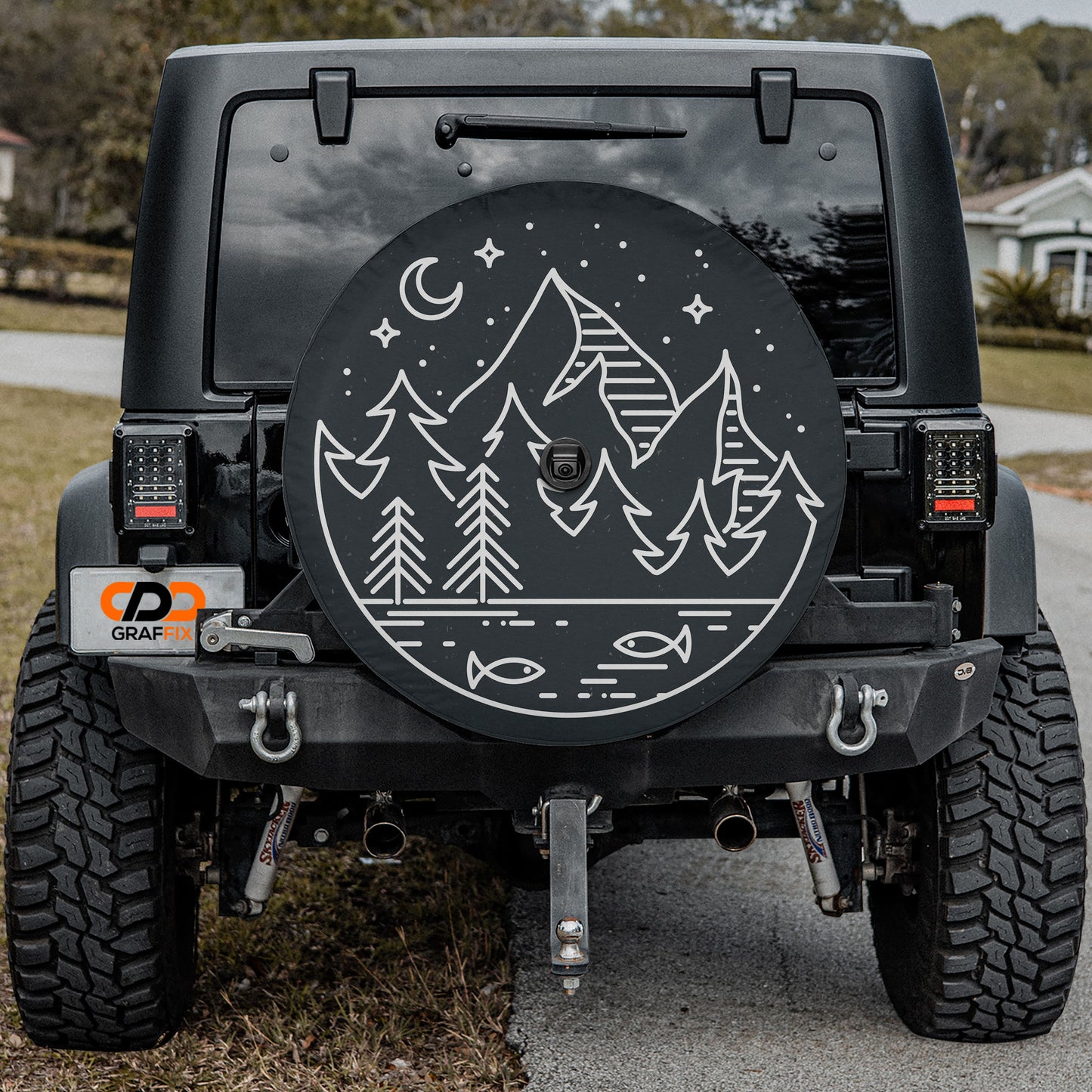 the back of a black Jeep Wrangler with a large, round spare tire cover featuring a mountain landscape design.