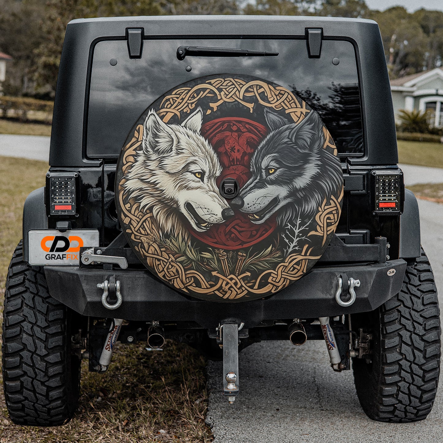 the rear of a black Jeep Wrangler with a large, decorative wheel cover featuring a design of two wolves facing each other.