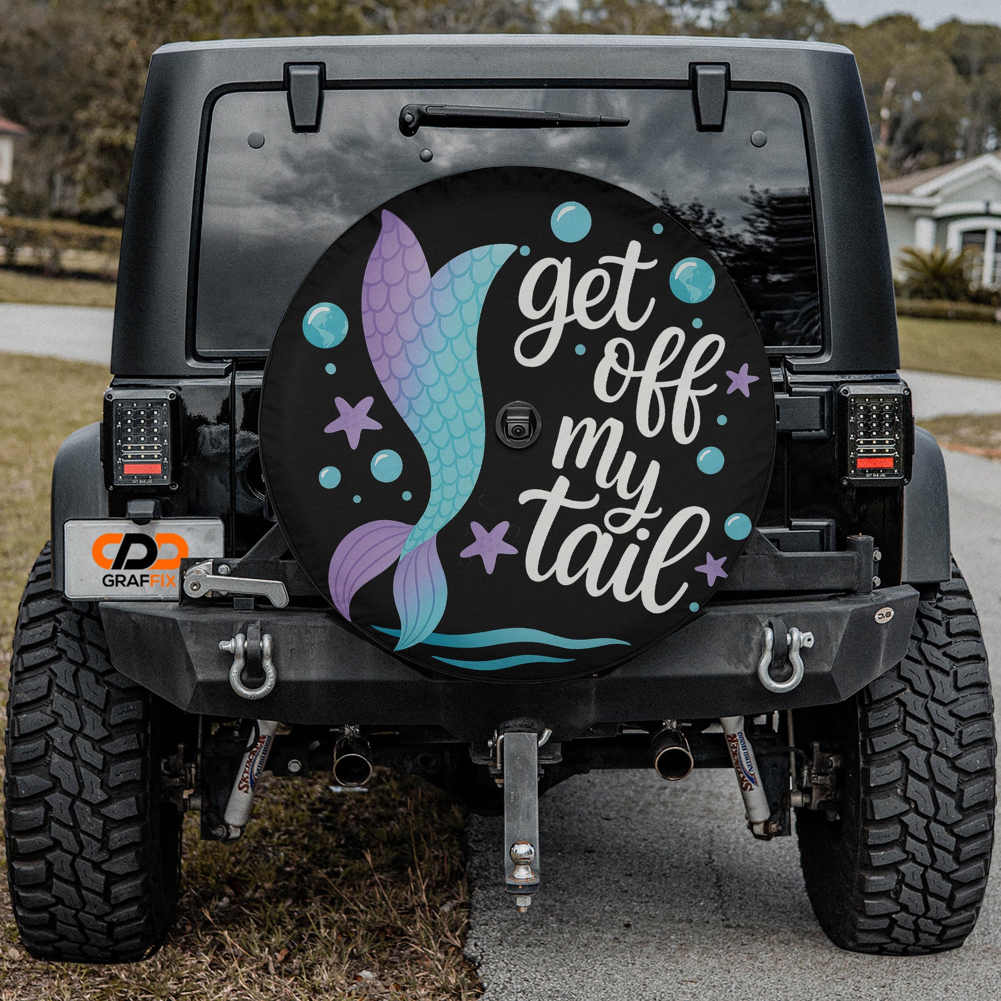 the rear of a black Jeep Wrangler with a large, colorful wheel cover featuring a mermaid design and the text "get off my tail".