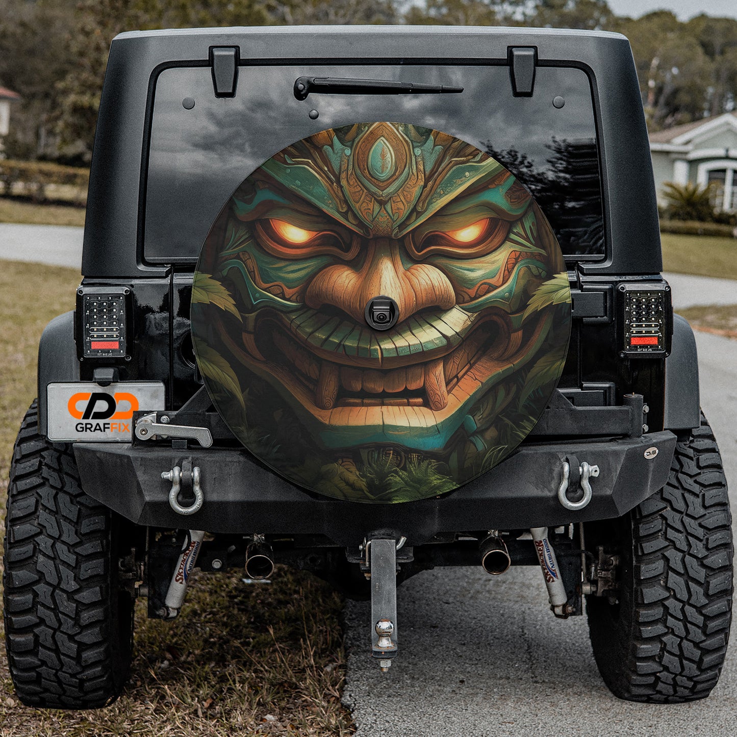 a black Jeep Wrangler with a large, colorful wheel cover depicting a dragon or mythical creature. The wheel cover is mounted on the rear of the Jeep, and the Jeep is parked on a road.