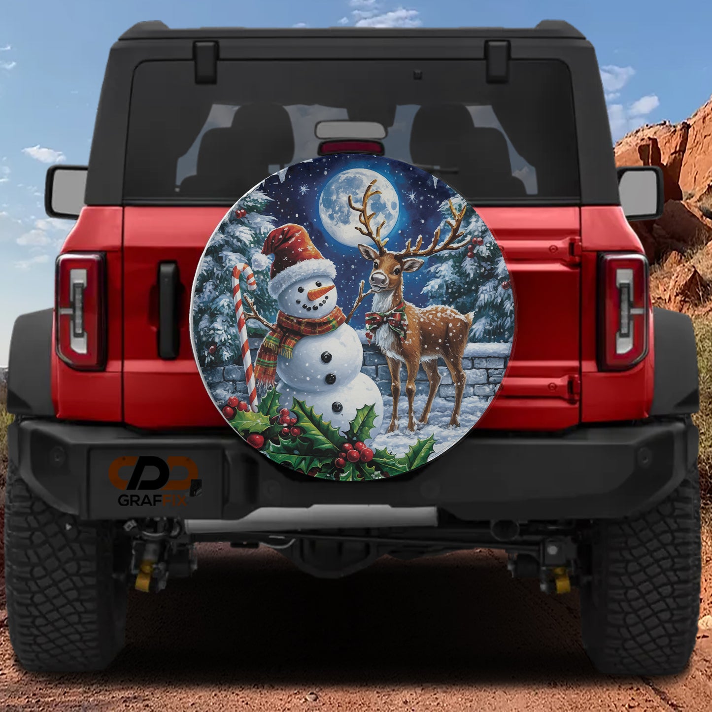 A red Jeep Wrangler with a snowman and deer decal on the rear window, set against a snowy mountain landscape.