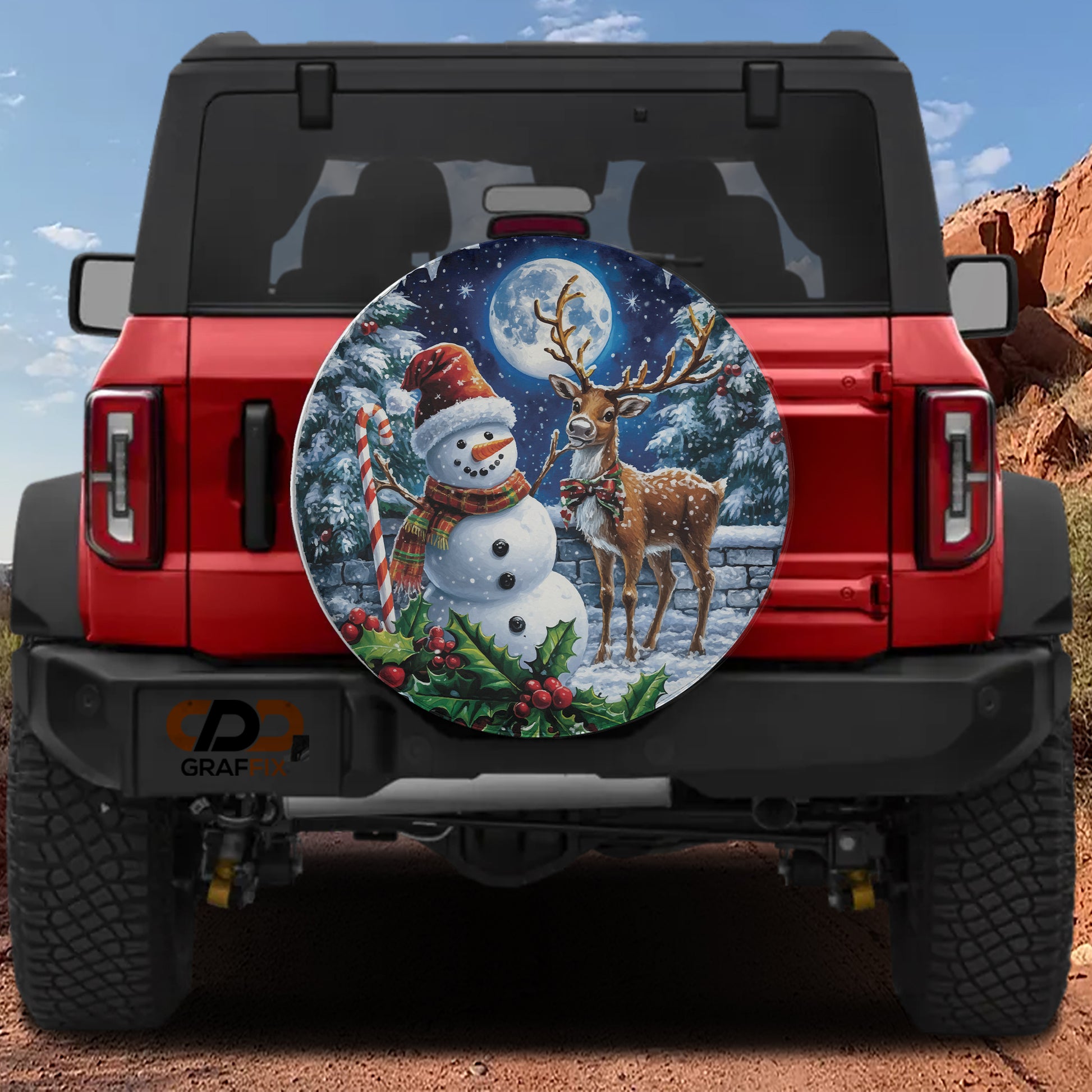 A red Jeep Wrangler with a snowman and deer decal on the rear window, set against a snowy mountain landscape.
