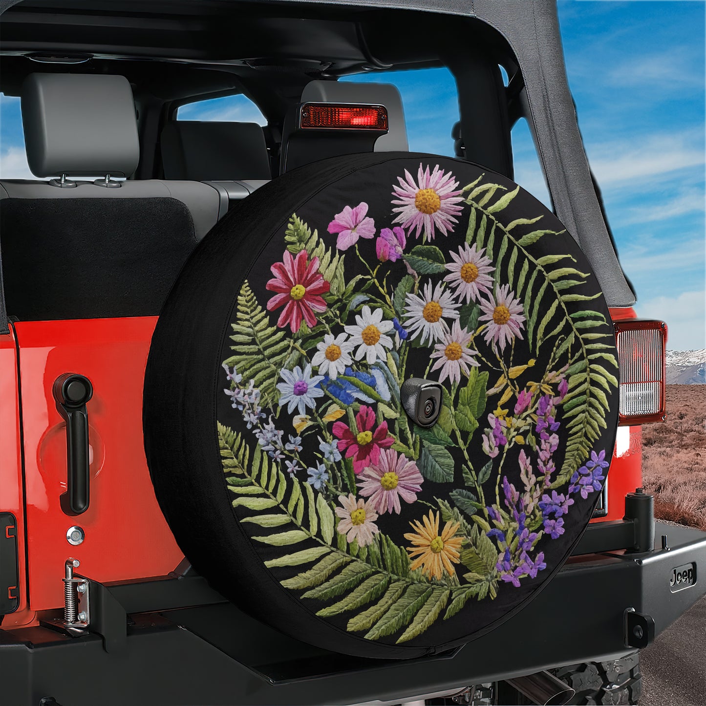 A colorful floral pattern on a spare tire attached to a red Jeep vehicle.