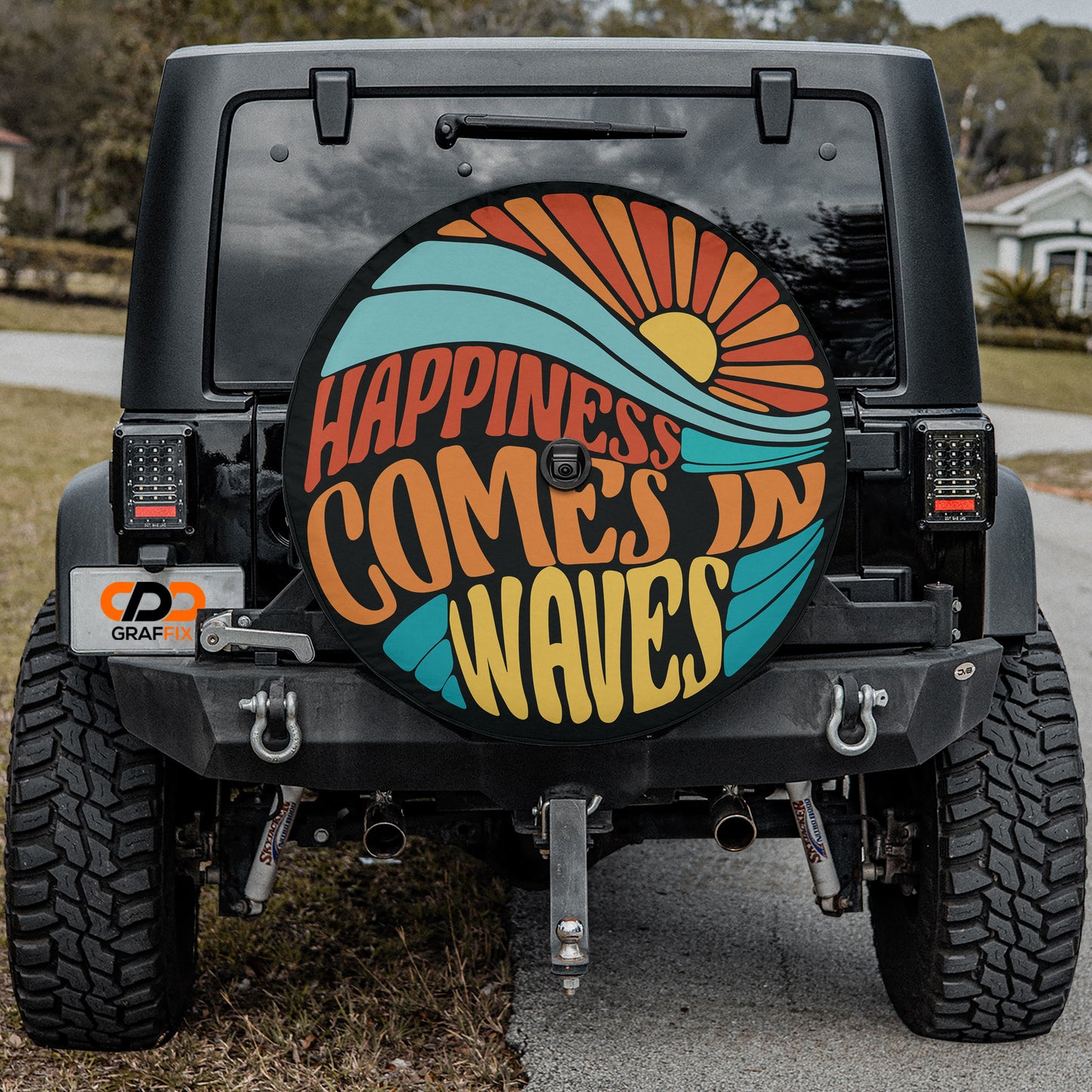 the back of a black Jeep Wrangler with a large, colorful wheel cover that says "Happiness comes in waves".
