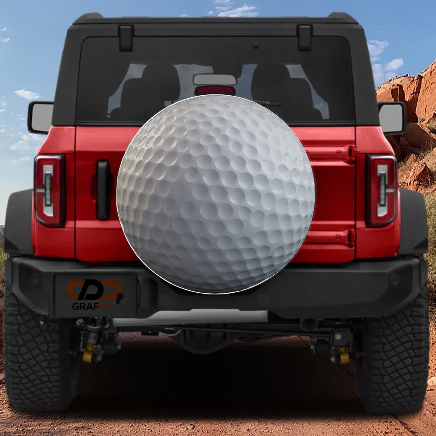 A red Jeep Wrangler with a large golf ball mounted on the rear bumper, set against a desert landscape with mountains in the background.