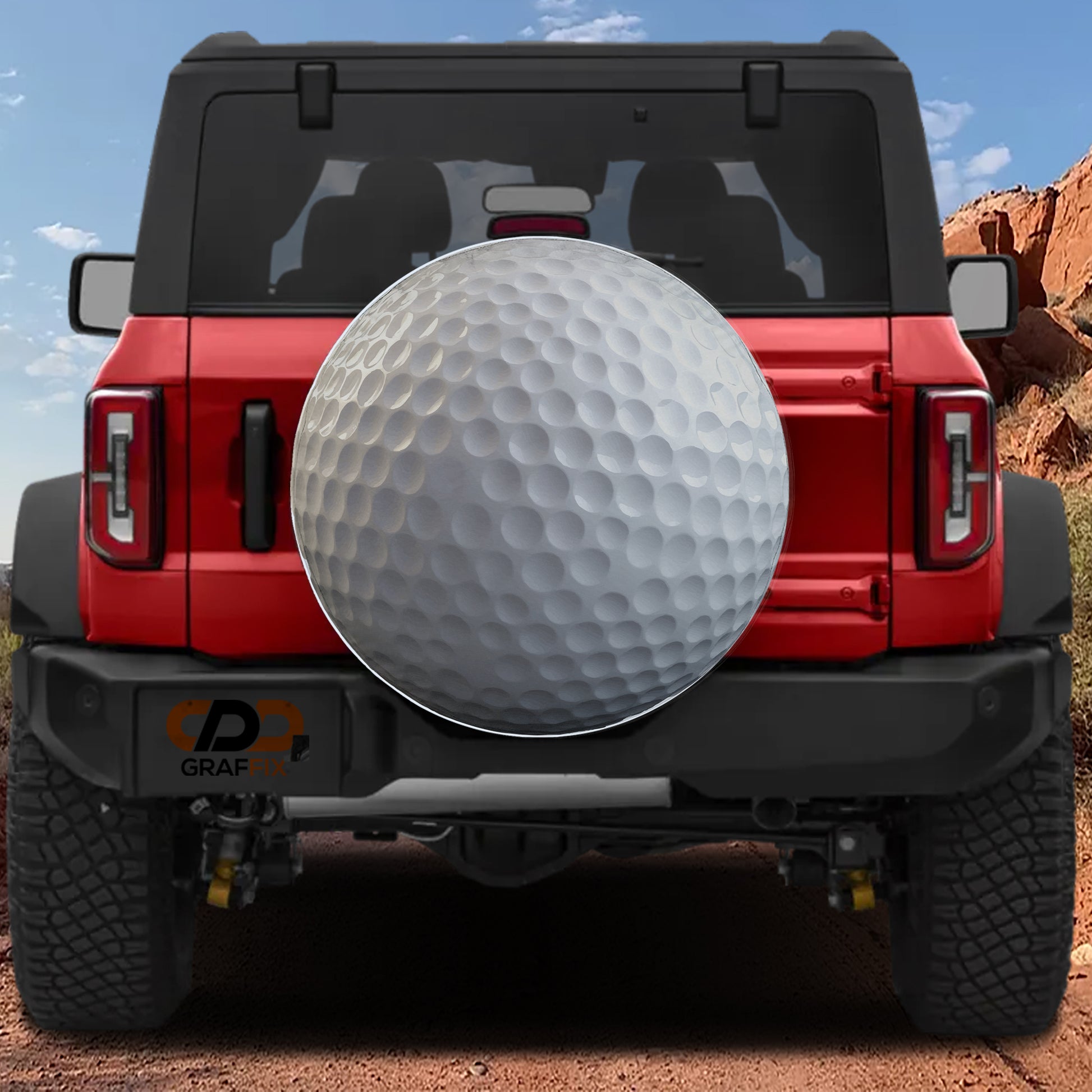 A red Jeep Wrangler with a large golf ball mounted on the rear bumper, set against a desert landscape with mountains in the background.