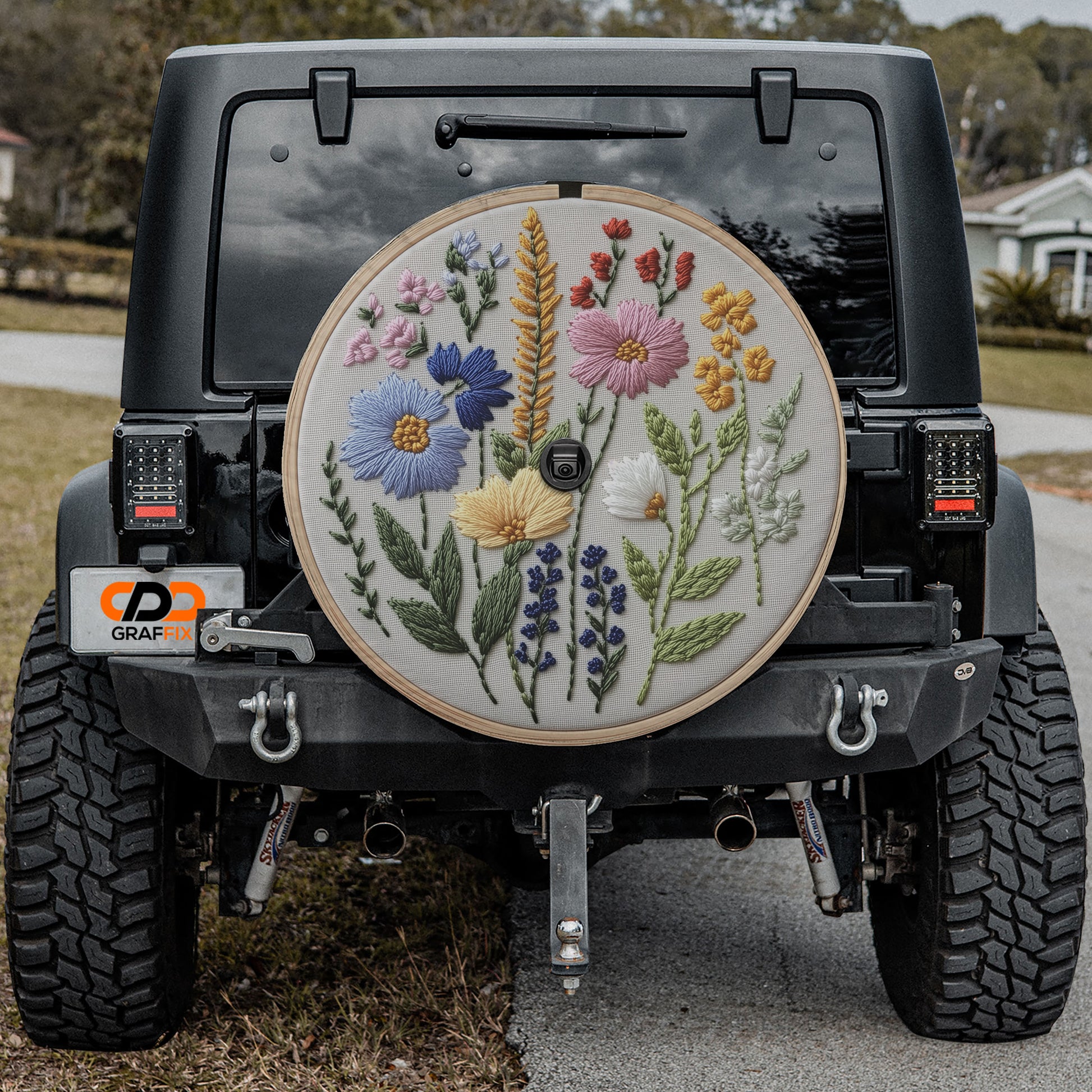 a black Jeep Wrangler with a large embroidered wheel cover featuring a floral design.