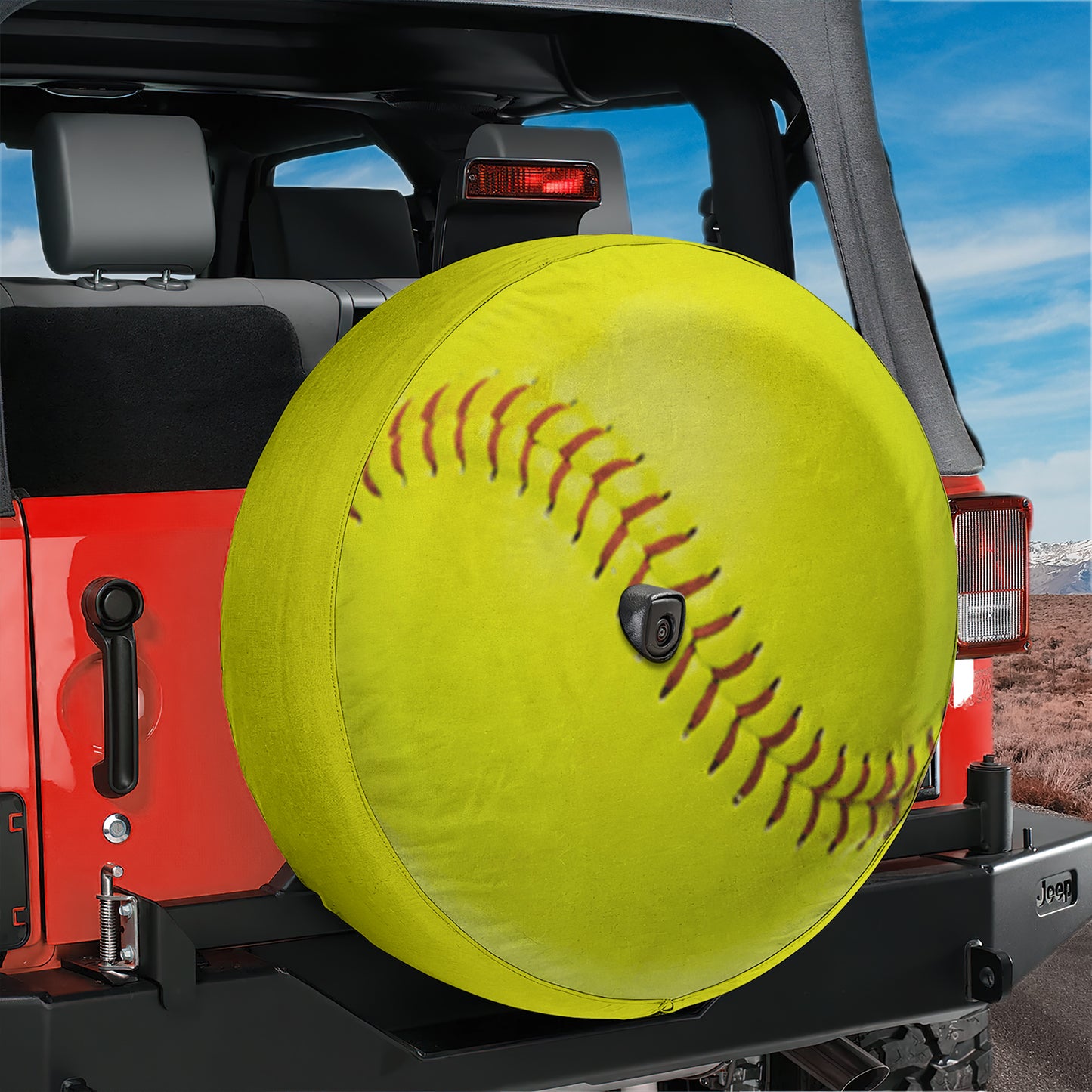 A large yellow softball with red stitching is mounted on the rear of a red Jeep, with a clear blue sky in the background.