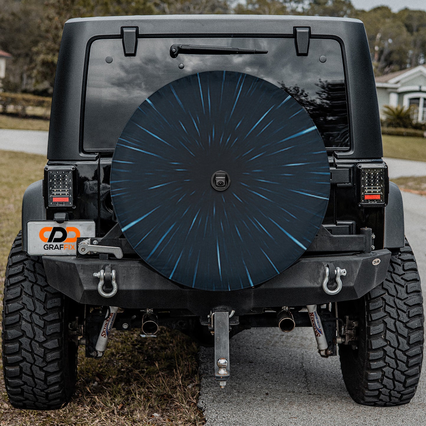 a black Jeep Wrangler parked on a road, with a large black tire cover attached to the rear of the vehicle.