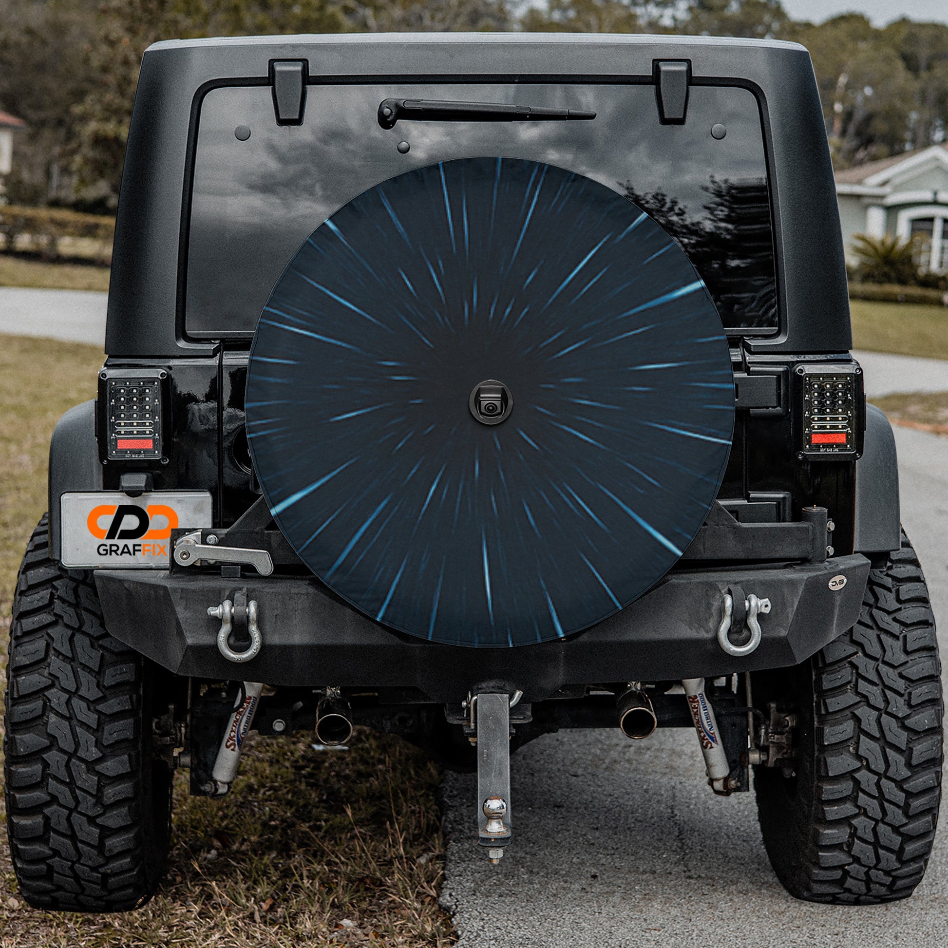 a black Jeep Wrangler parked on a road, with a large black tire cover attached to the rear of the vehicle.