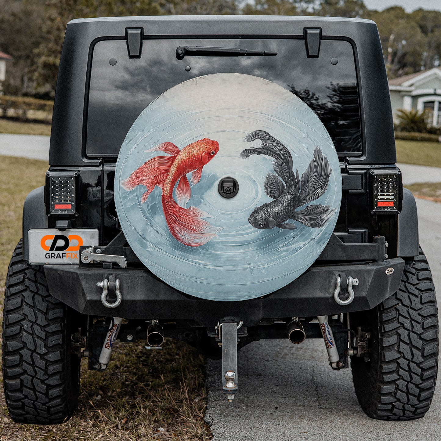 the rear of a black Jeep Wrangler with a large, round spare tire attached to the vehicle. The spare tire features a design of two fish, one red and one black, swimming in a blue and white circular pattern.