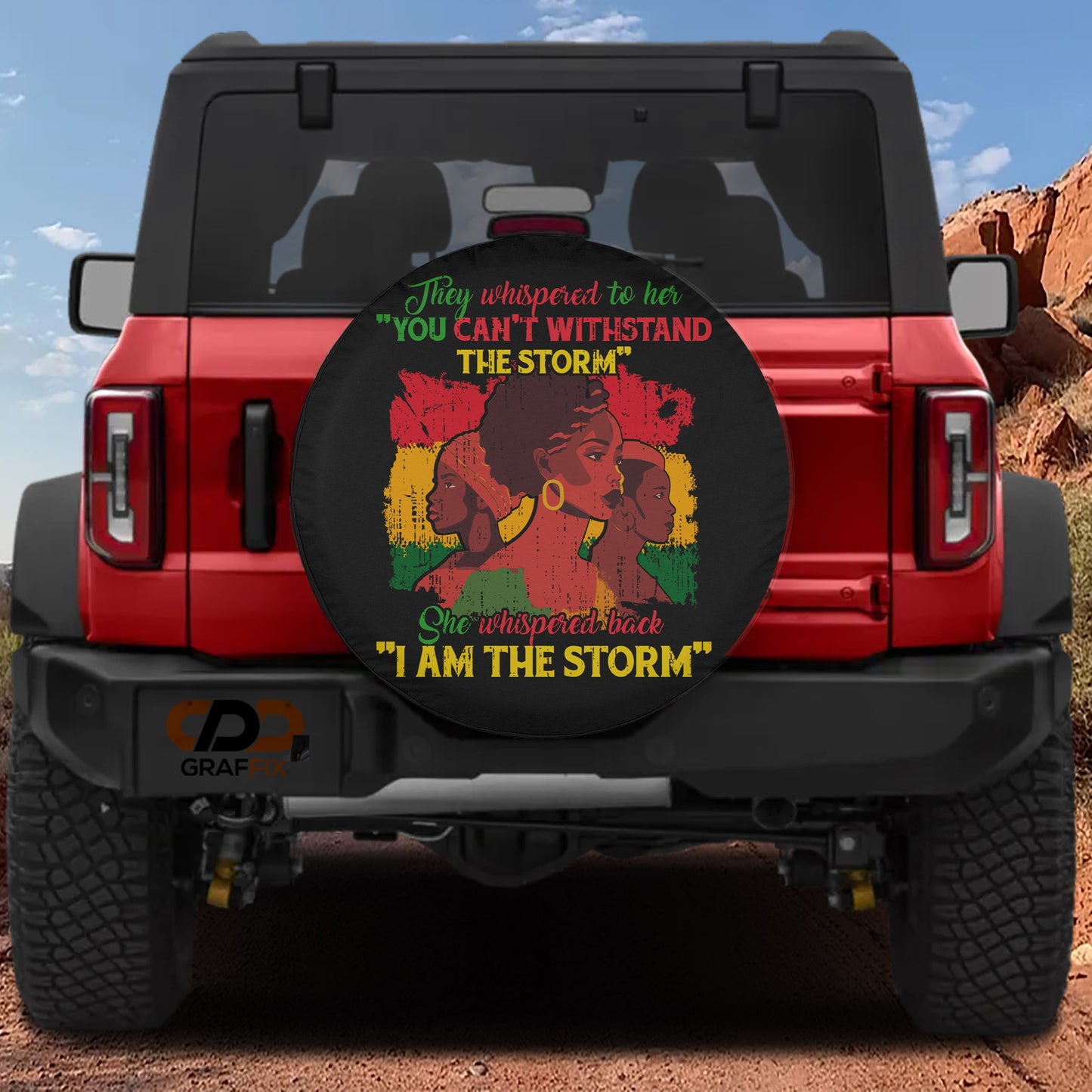 a red Jeep Wrangler with a large wheel cover featuring a graphic of a woman with dreadlocks and the text "They whispered to her 'You can't withstand the storm' She whipped back 'I am the storm'".
