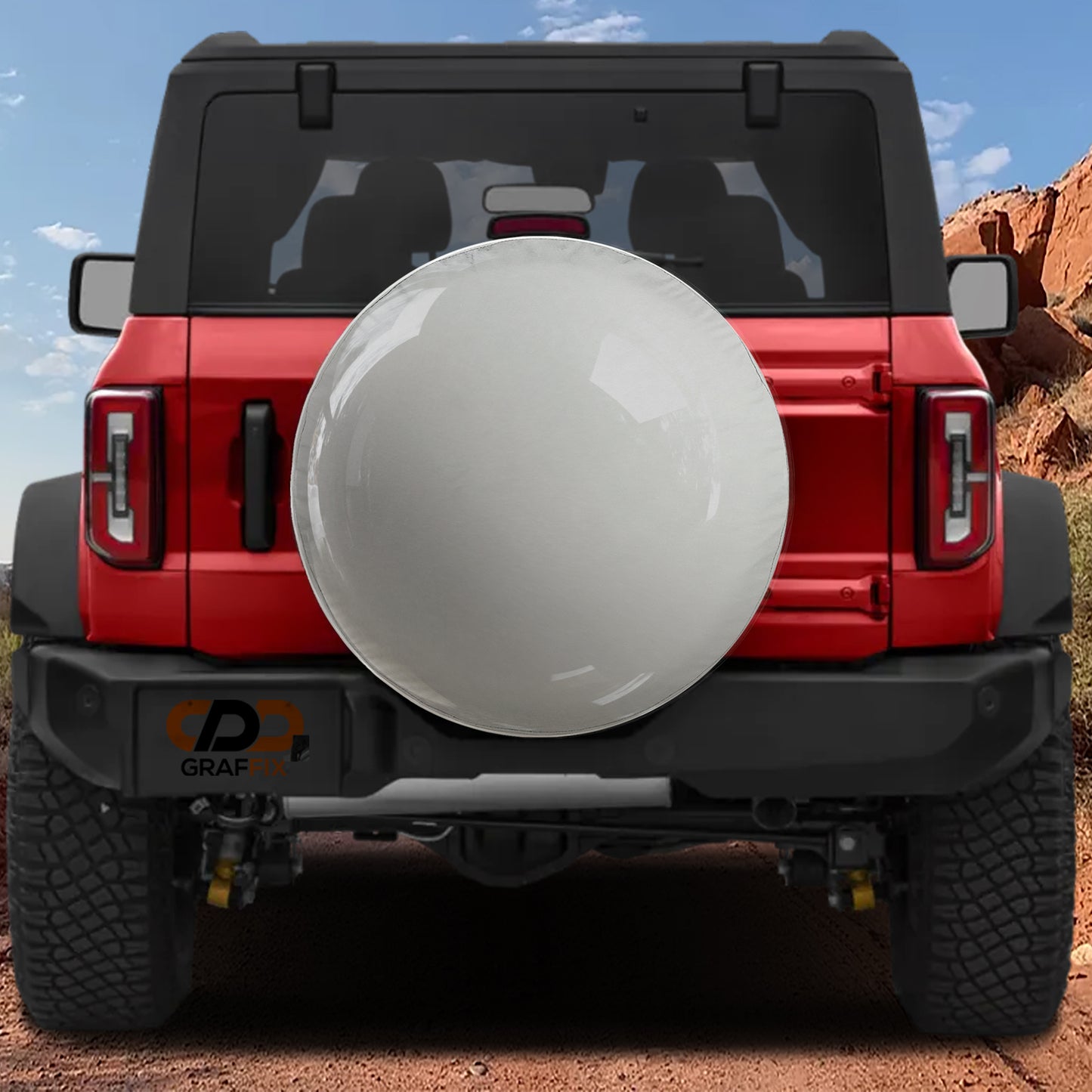 A red Jeep Wrangler with a large white tire cover attached to the rear of the vehicle, parked on a dirt road with a rocky hill in the background.