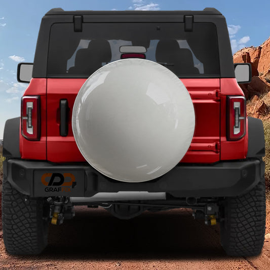 A red Jeep Wrangler with a large white tire cover attached to the rear of the vehicle, parked on a dirt road with a rocky hill in the background.