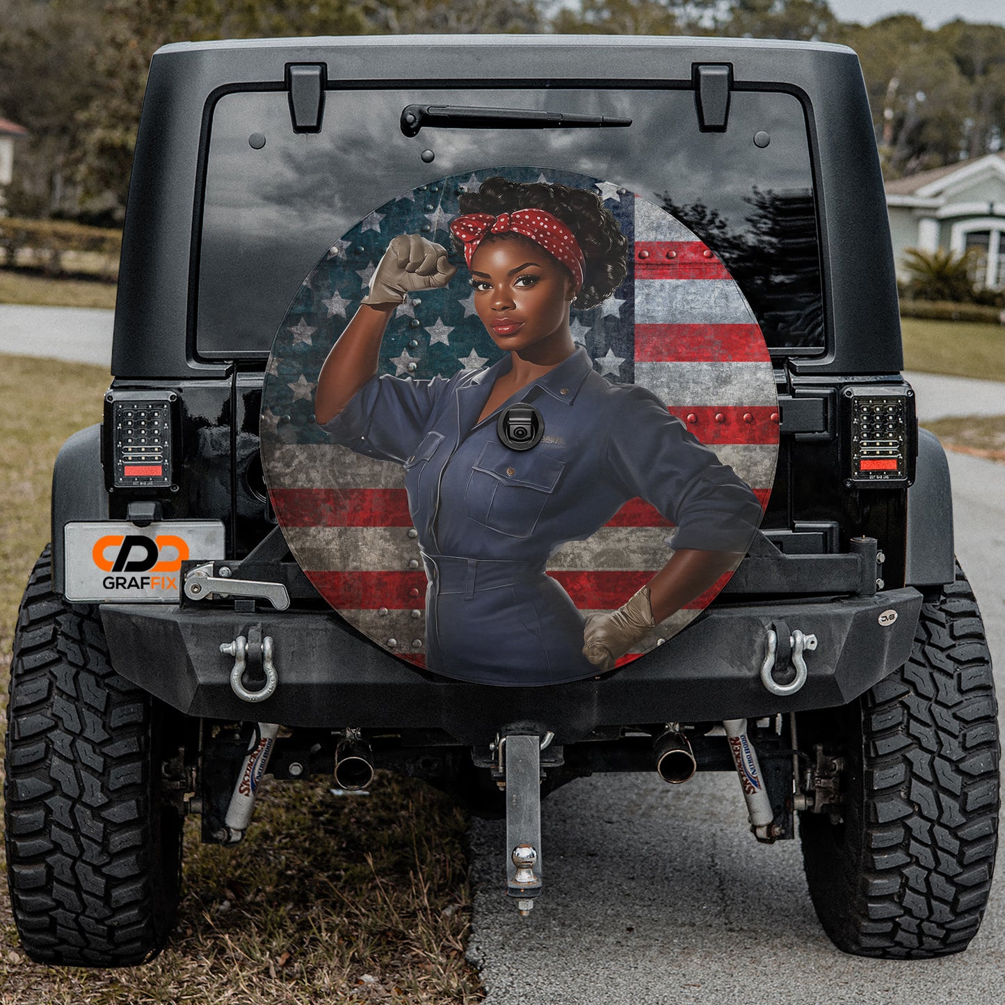 a woman with a determined expression, wearing a blue jumpsuit and a red bandana, standing in front of an American flag.