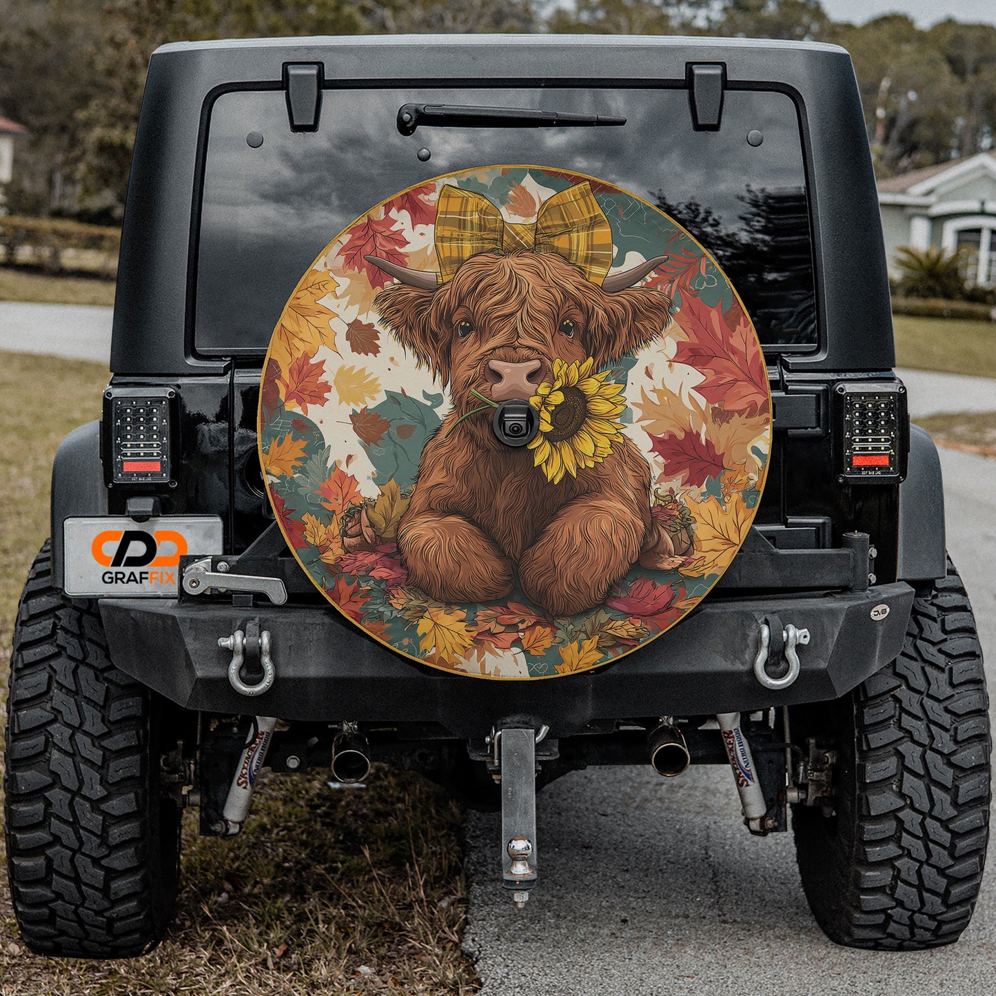 a black Jeep Wrangler with a large, colorful wheel cover depicting a cow with a bow on its head.