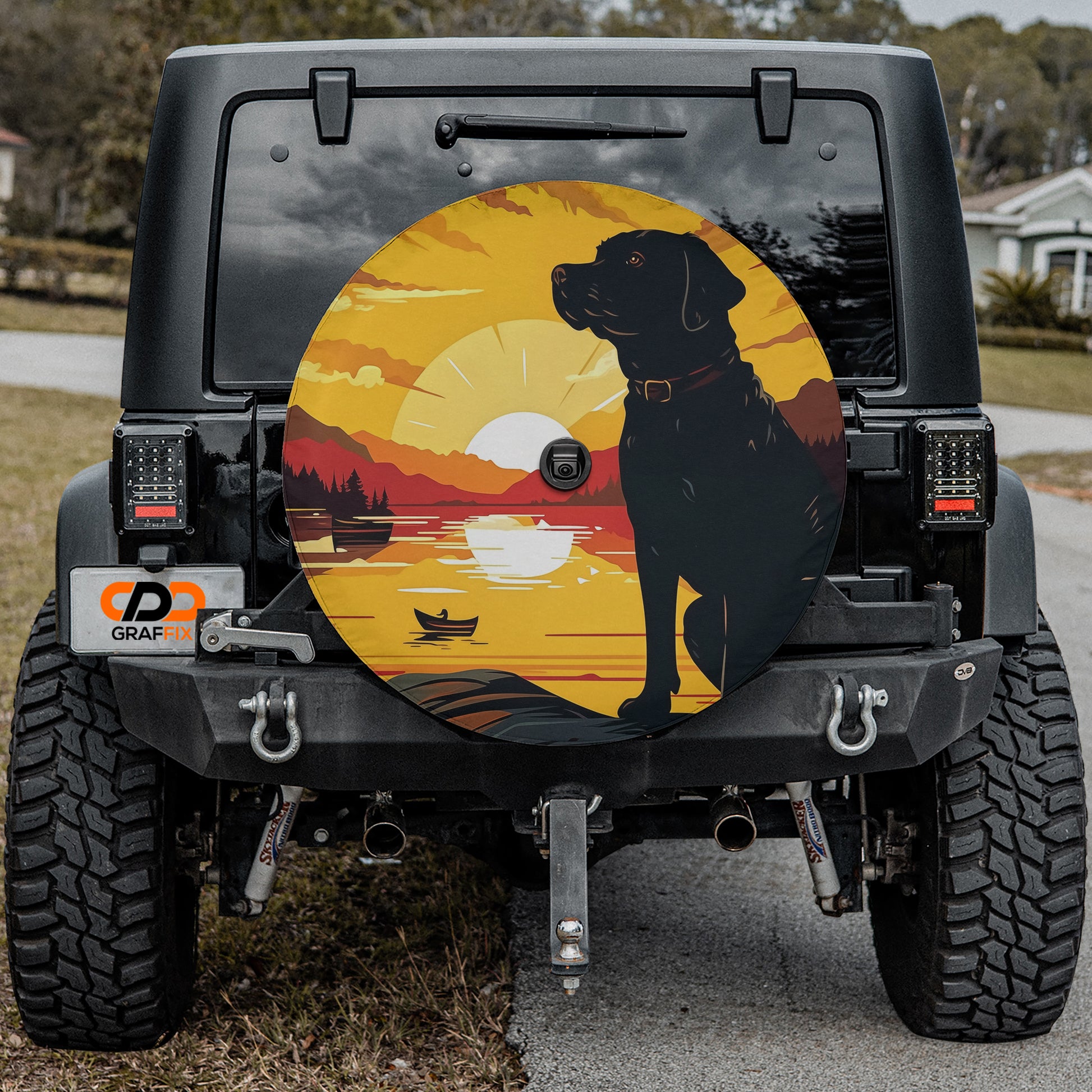 a black dog sitting on a road, with a sunset and a boat in the background.