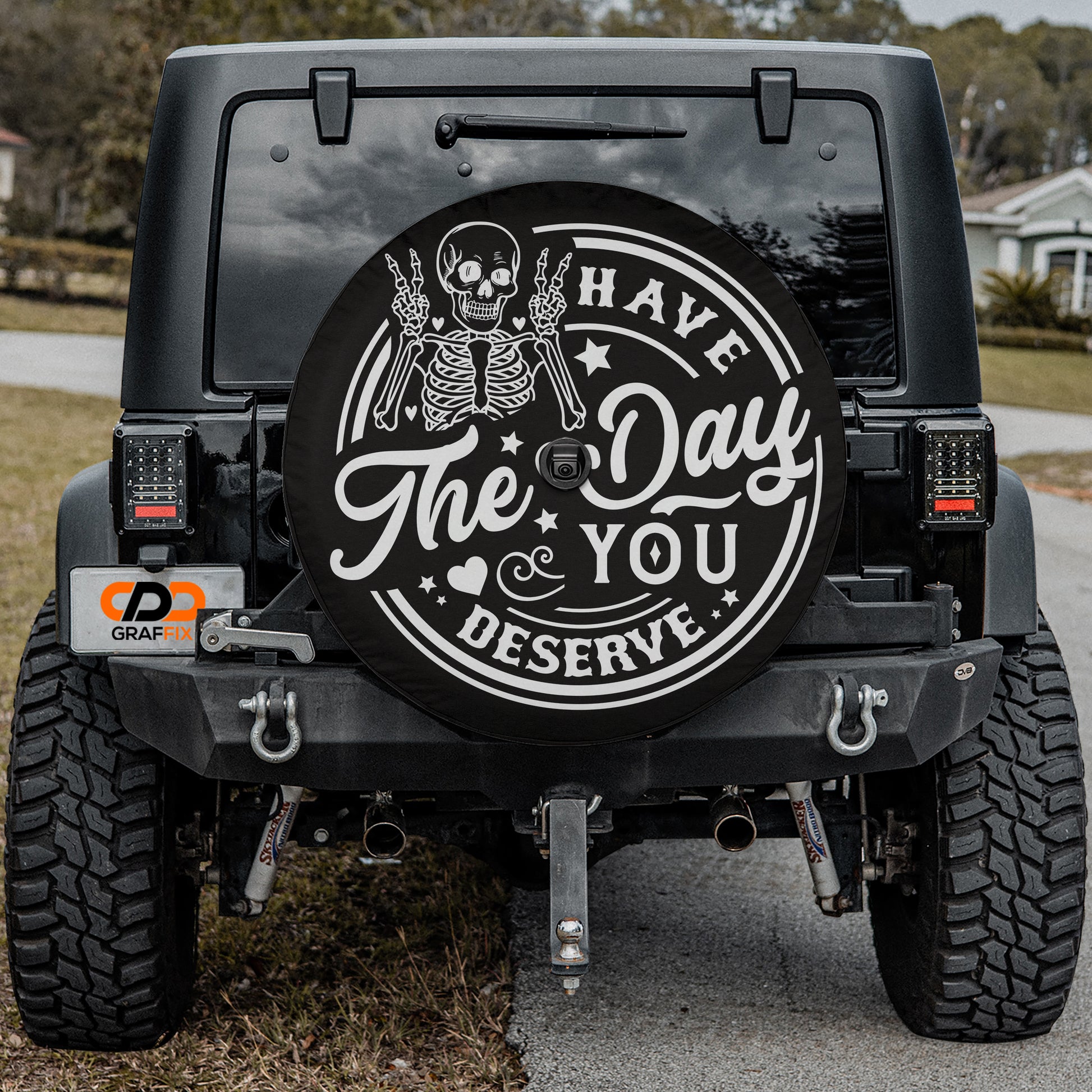 the back of a black Jeep Wrangler with a large black tire cover featuring a skeleton and the text "Have a Day, You Deserve".