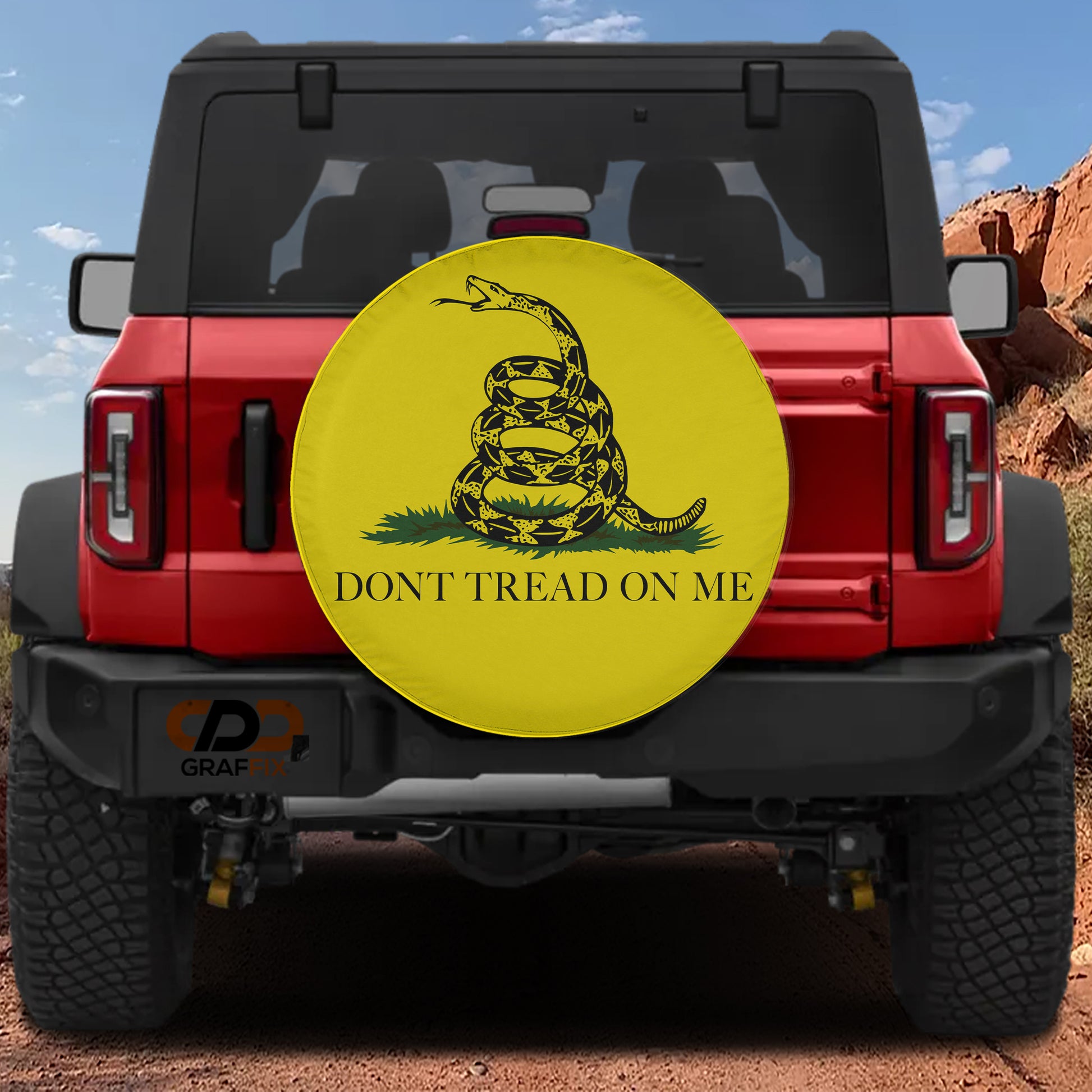 a red Jeep Wrangler with a large yellow wheel cover on the rear of the vehicle. The wheel cover displays a black and yellow design of a snake wrapped around the text "DON'T TREAD ON ME".