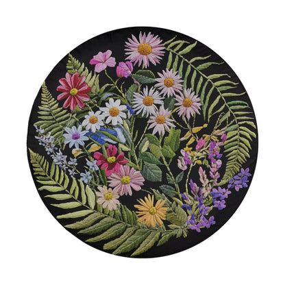 The image is a circular arrangement of various colorful flowers and leaves, including daisies, chrysanthemums, and ferns, all set against a black background.