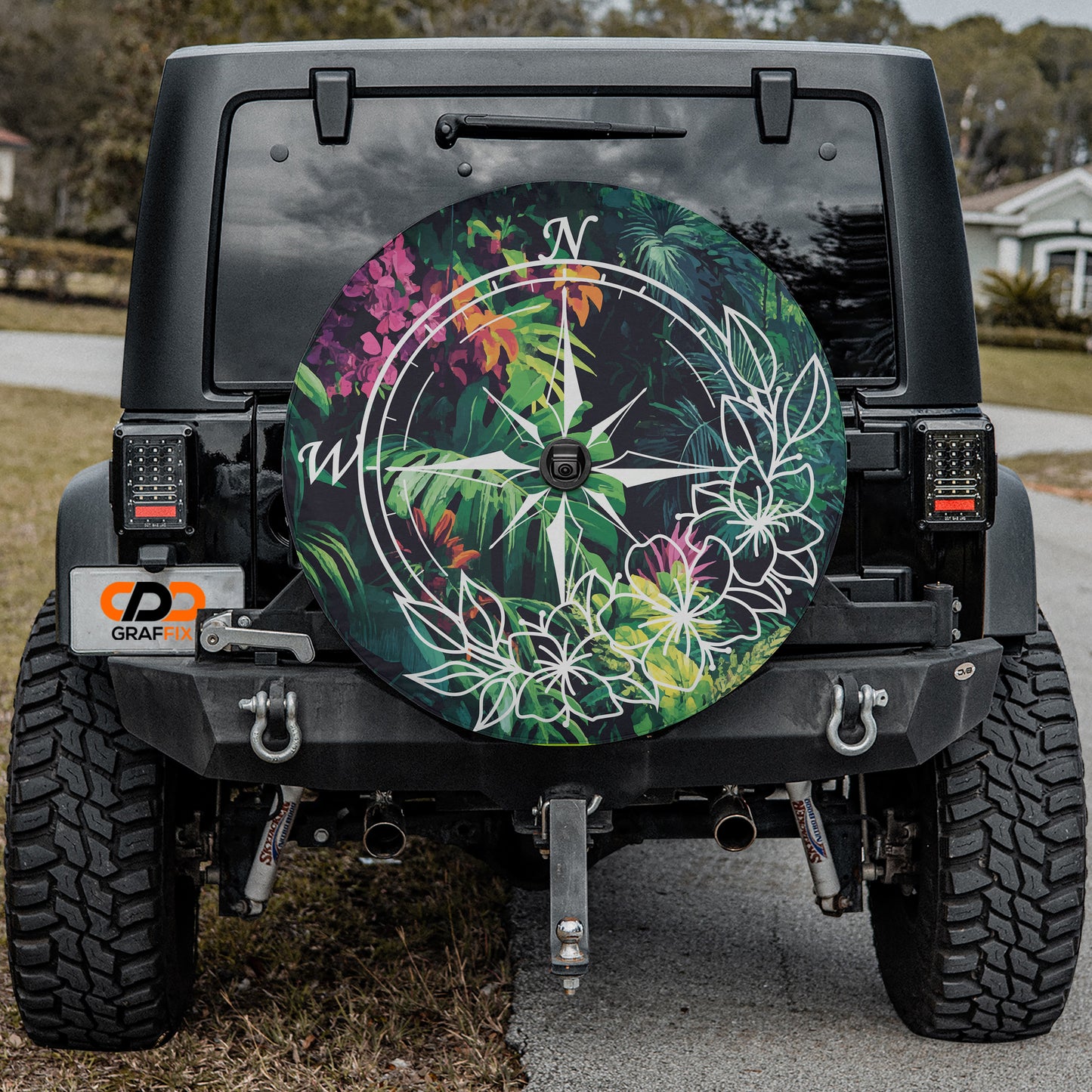 the back of a black Jeep Wrangler with a large, colorful wheel cover featuring a compass design and tropical flowers.