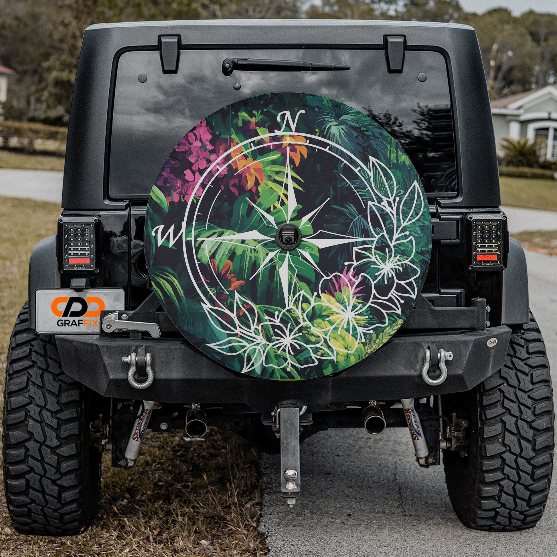 the back of a black Jeep Wrangler with a large, colorful wheel cover featuring a compass design and tropical flowers.