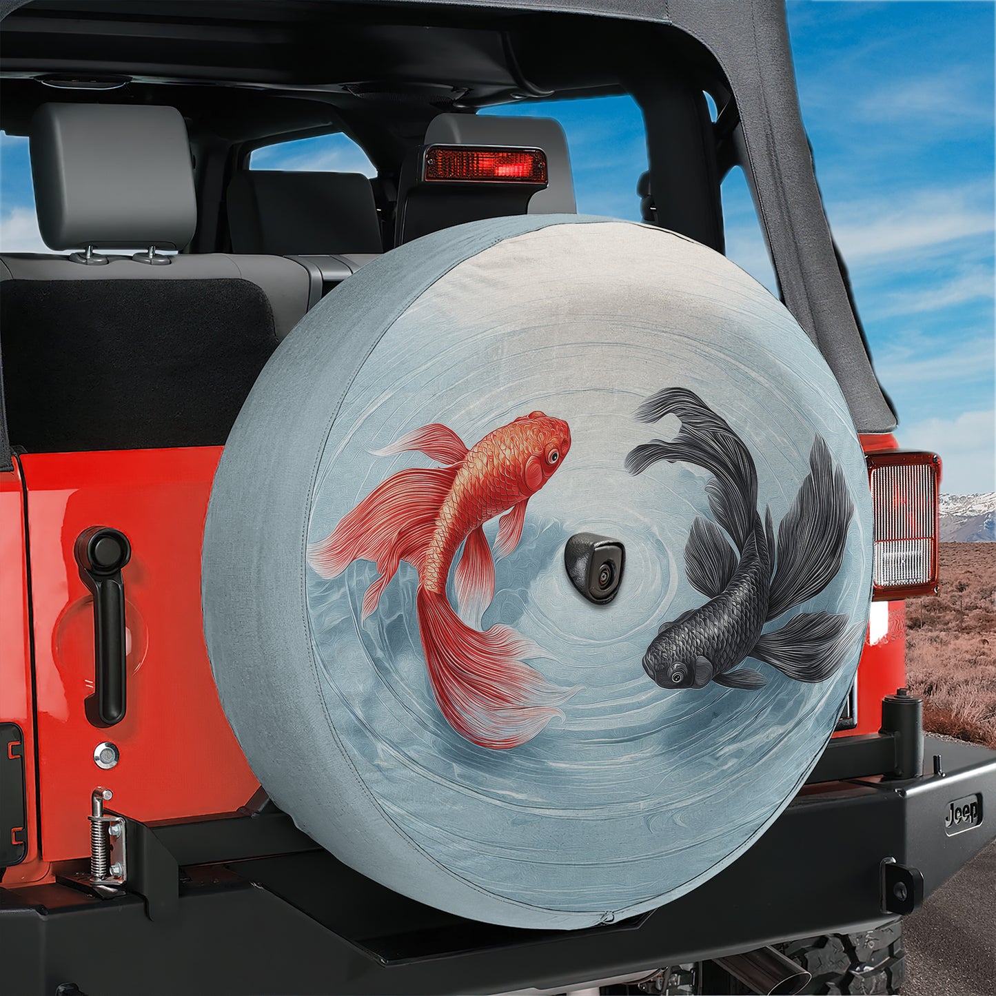 A red Jeep with a large tire cover featuring a fish design, including a red fish and a black fish, is parked in a desert-like environment.