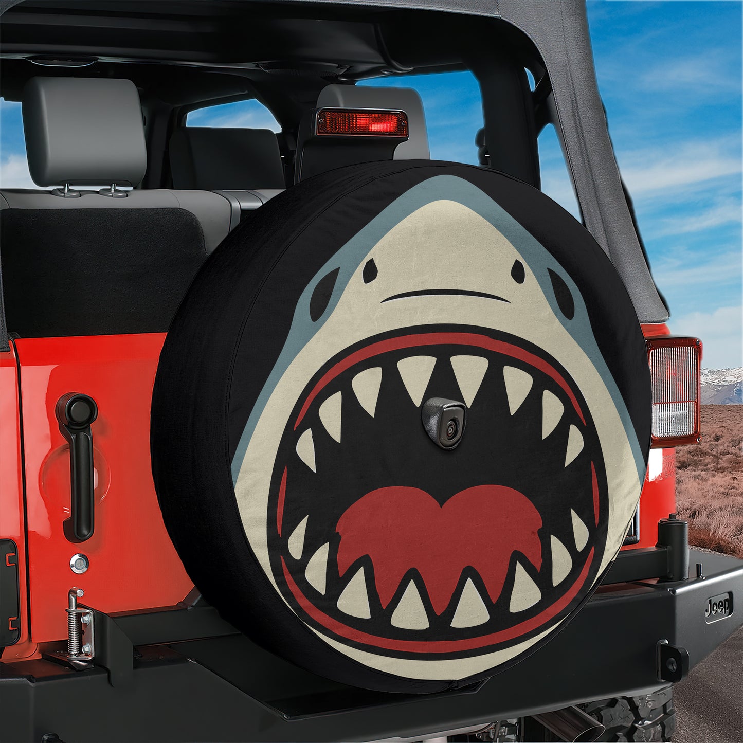 A red Jeep Wrangler with a shark-themed spare tire cover attached to the rear of the vehicle.