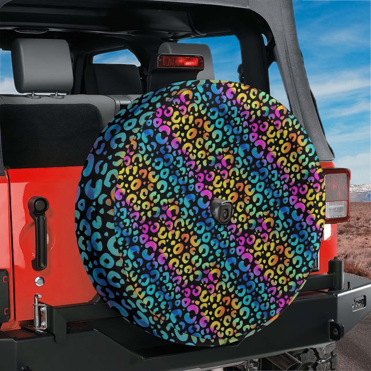 A colorful, leopard print spare tire cover is attached to the rear of a red Jeep vehicle, with a desert landscape visible in the background.