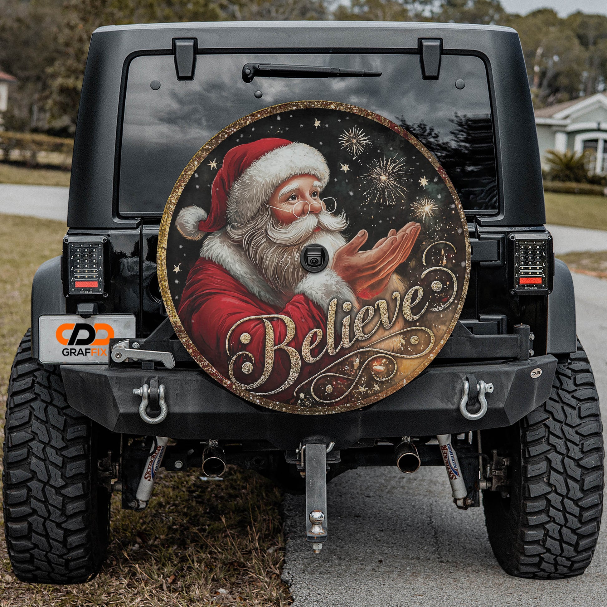 a black Jeep Wrangler with a large, round, and decorative wheel cover featuring a Santa Claus image and the word "Believe" written on it.