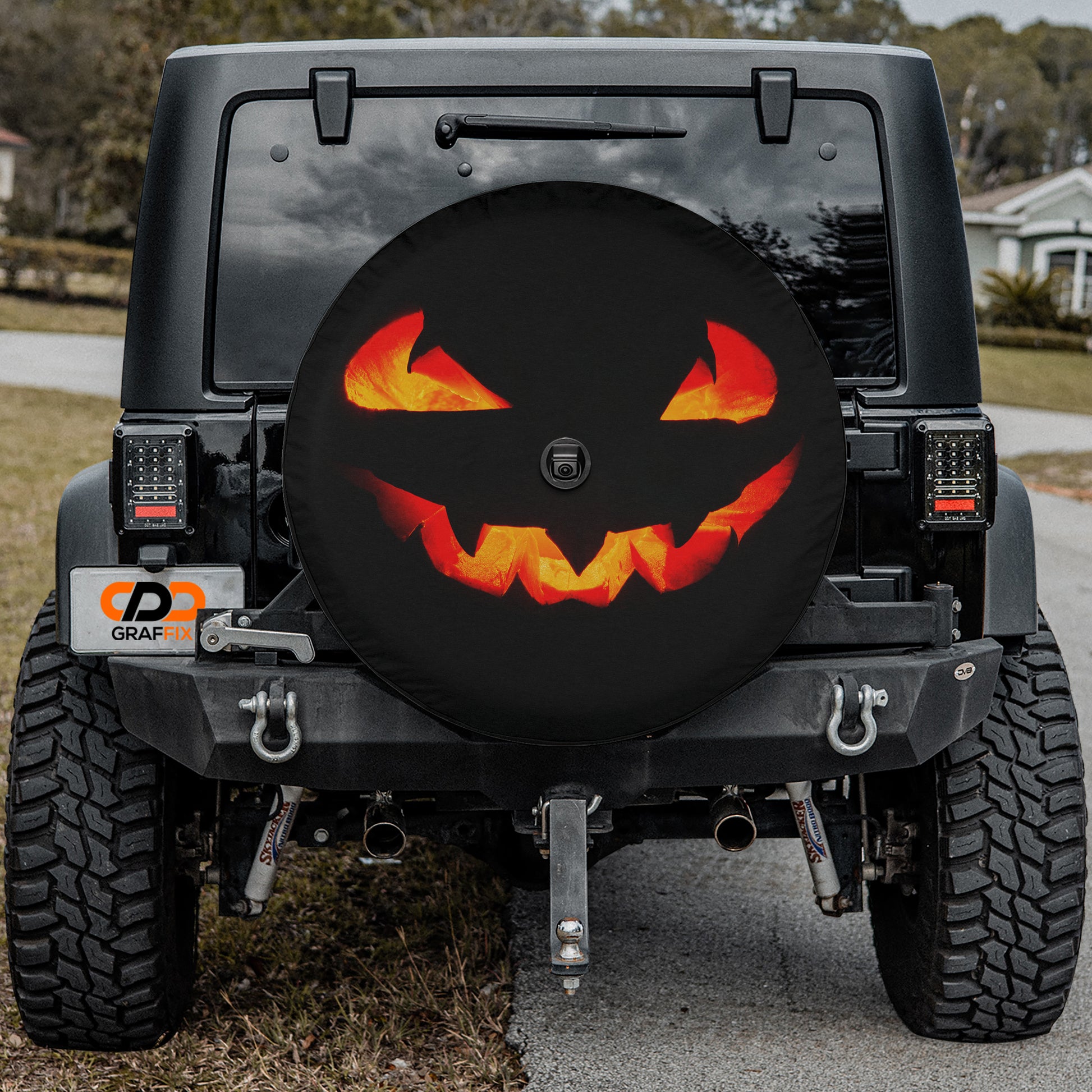 a black Jeep Wrangler with a Halloween-themed spare tire cover featuring a jack-o-lantern design.