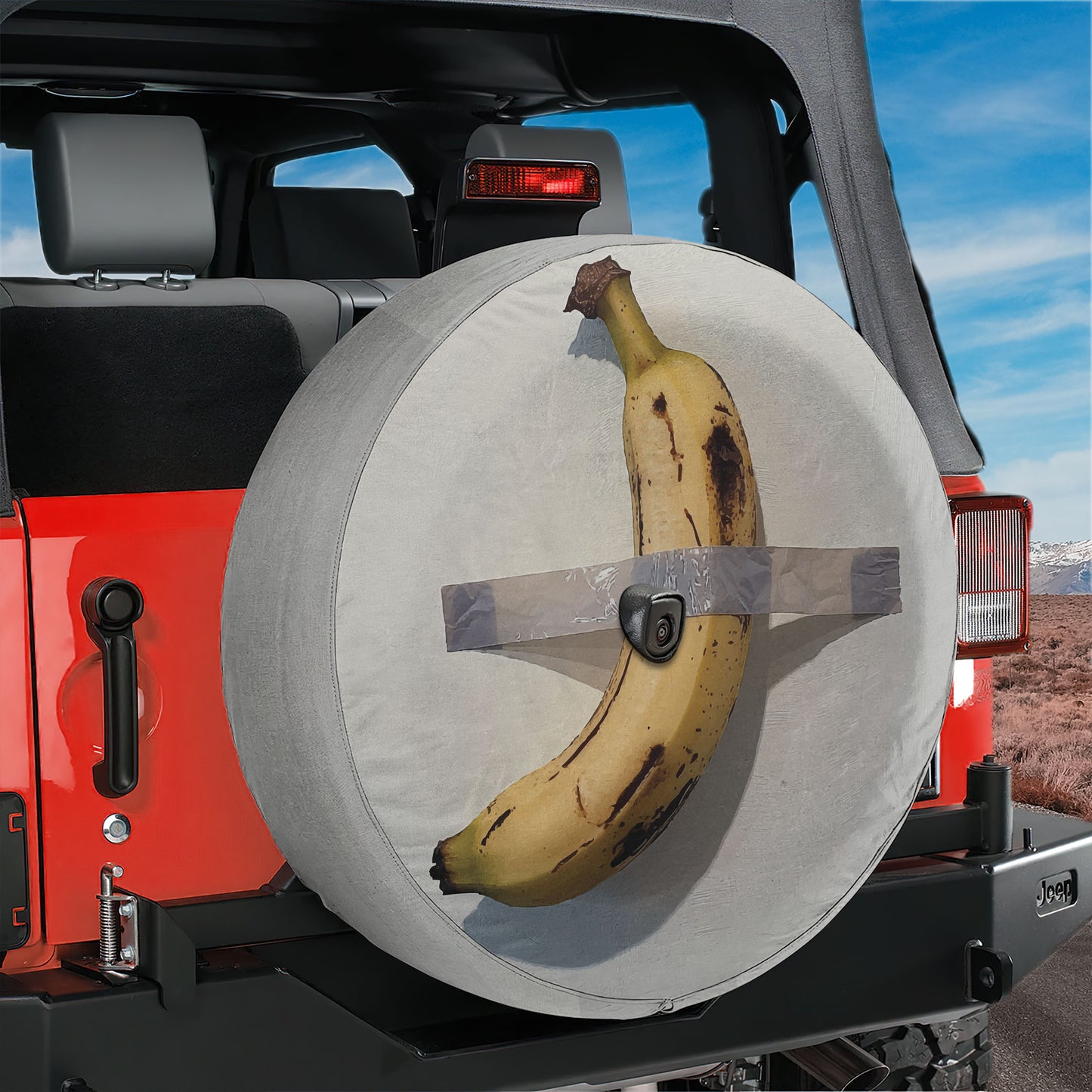 A banana is strapped to the spare tire of a Jeep, with the tire cover secured with duct tape.