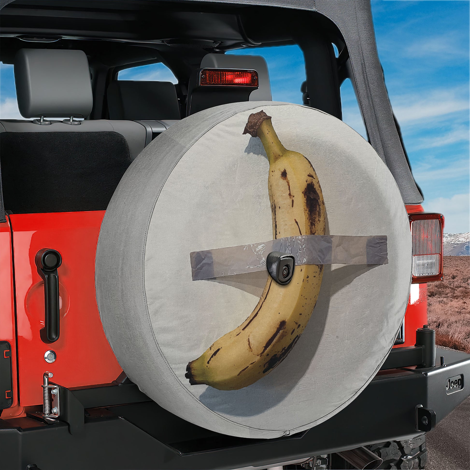 A banana is strapped to the spare tire of a Jeep, with the tire cover secured with duct tape.