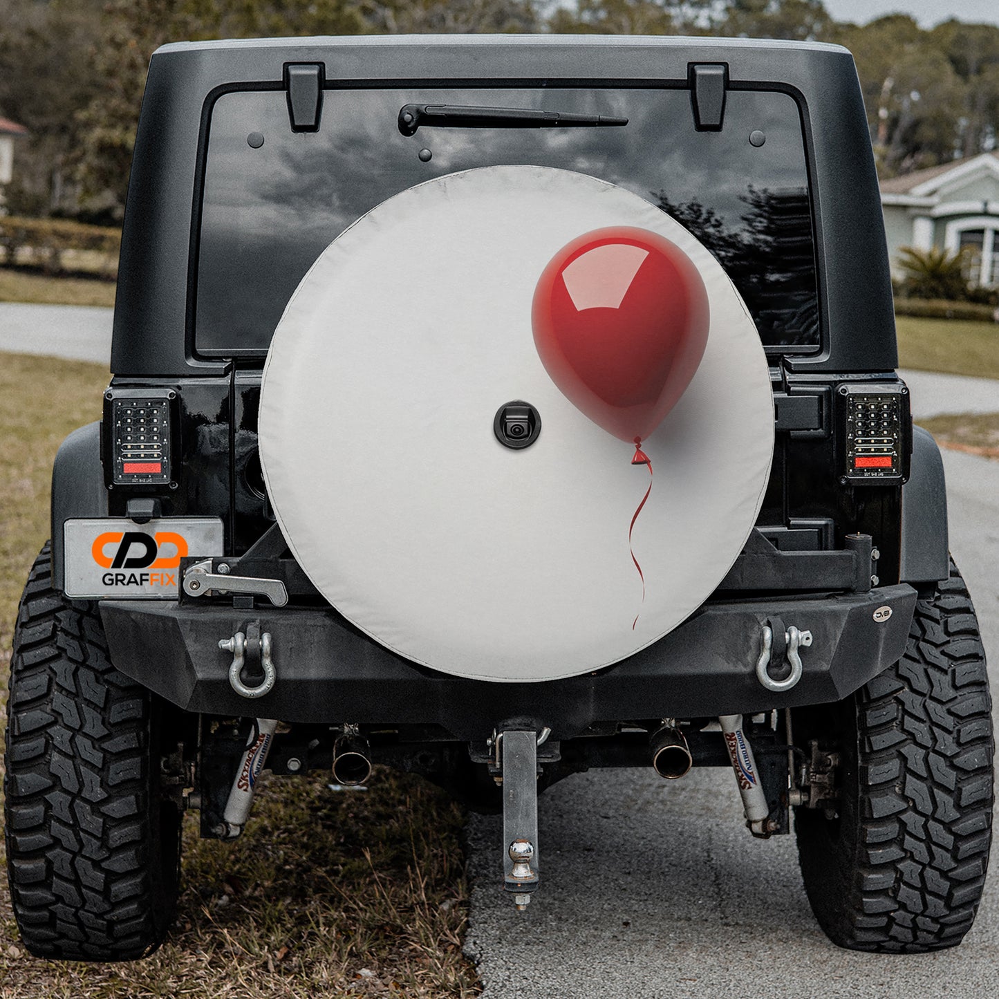 a black Jeep Wrangler with a large white tire cover attached to the rear of the vehicle. The tire cover has a red balloon attached to it, giving the impression of a festive or celebratory decoration.
