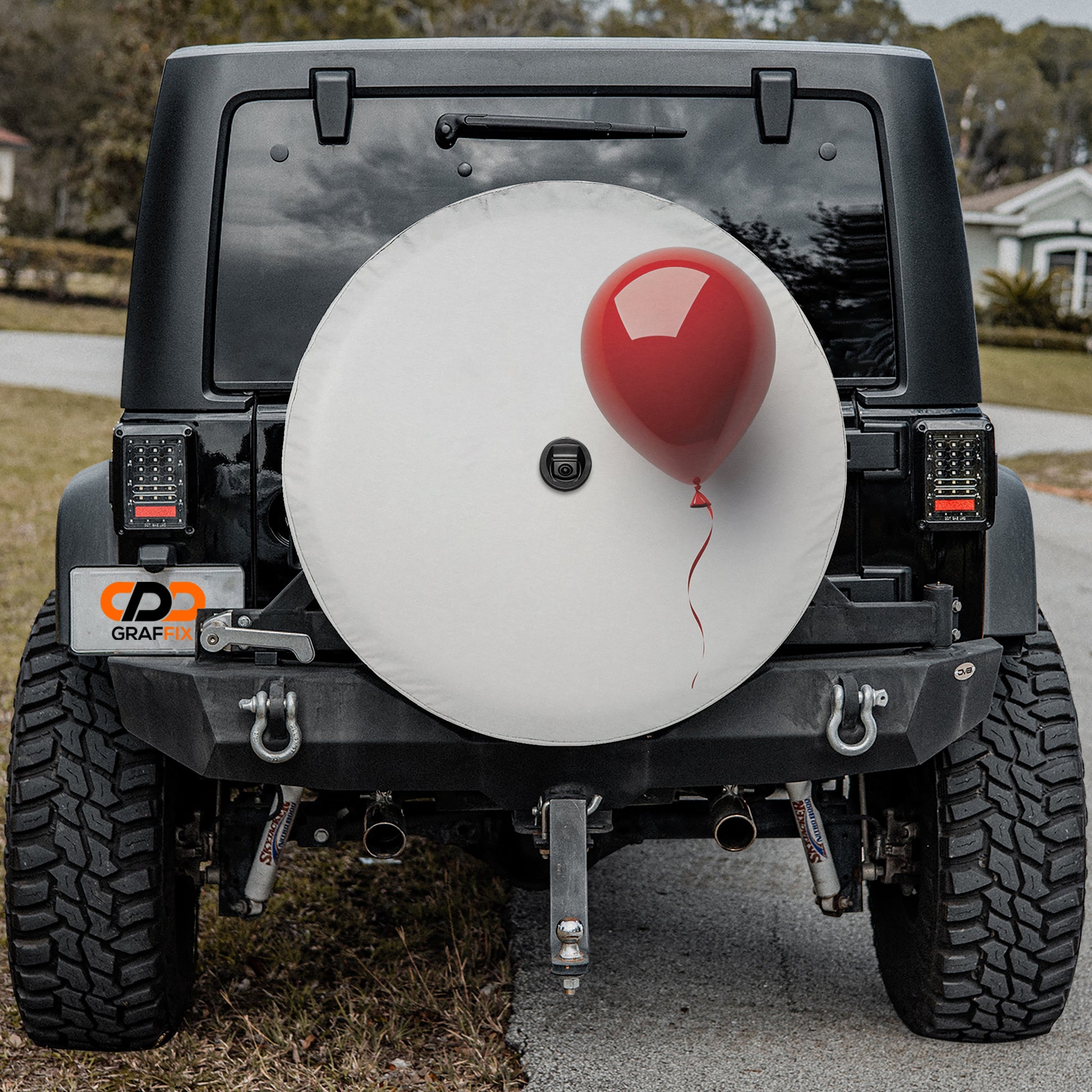 a black Jeep Wrangler with a large white tire cover attached to the rear of the vehicle. The tire cover has a red balloon attached to it, giving the impression of a festive or celebratory decoration.