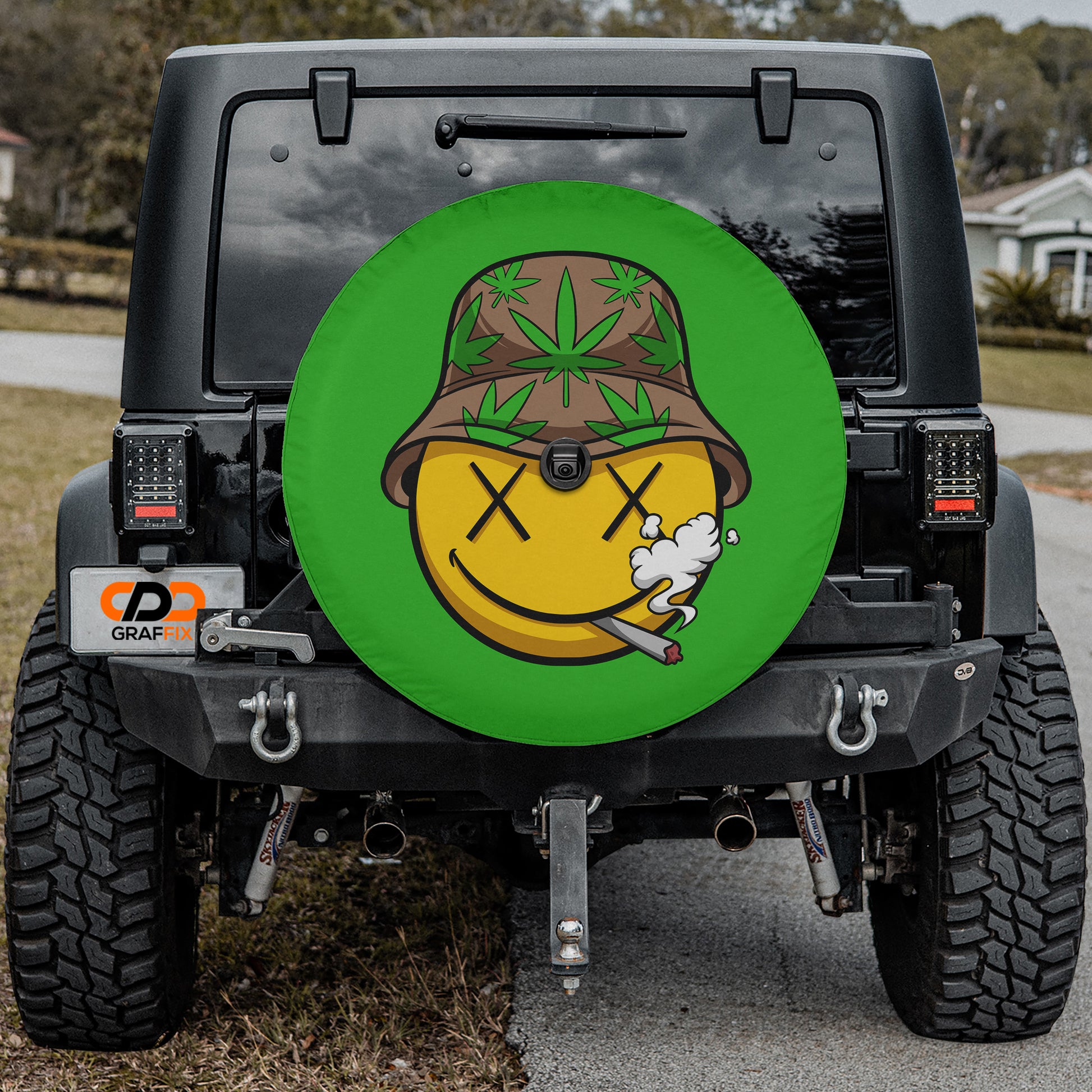 a black Jeep Wrangler with a large green tire cover featuring a cartoon smiley face and a weed in its mouth.