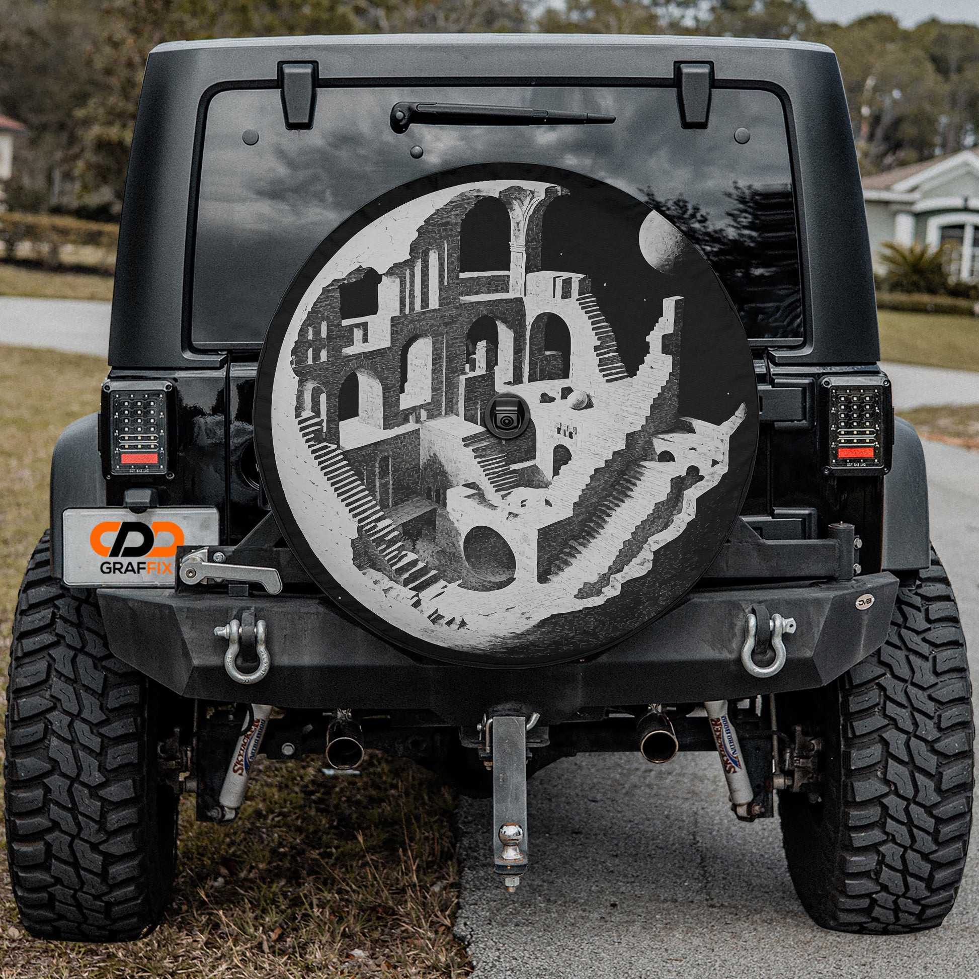the back of a black Jeep Wrangler with a large, round spare tire attached to it. The spare tire features an artistic design depicting a castle or palace-like structure.