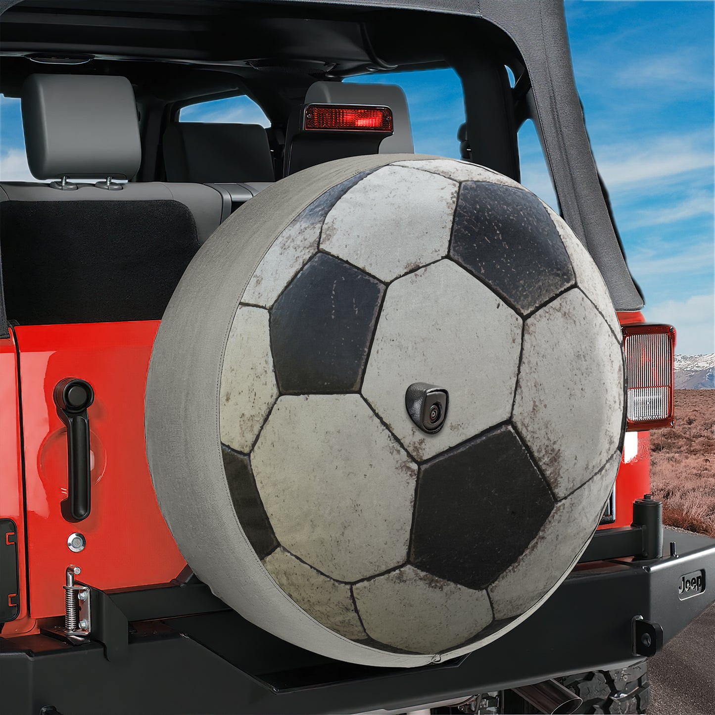 A red Jeep Wrangler with a large soccer ball mounted on the rear tire.